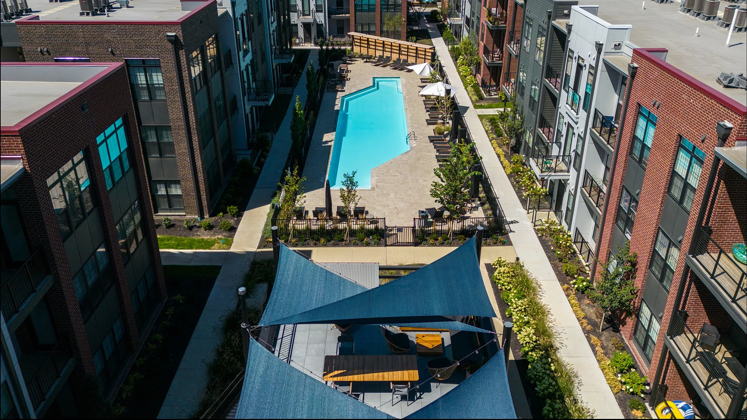 Aerial view of a stylish apartment complex with a central swimming pool and a sun deck.