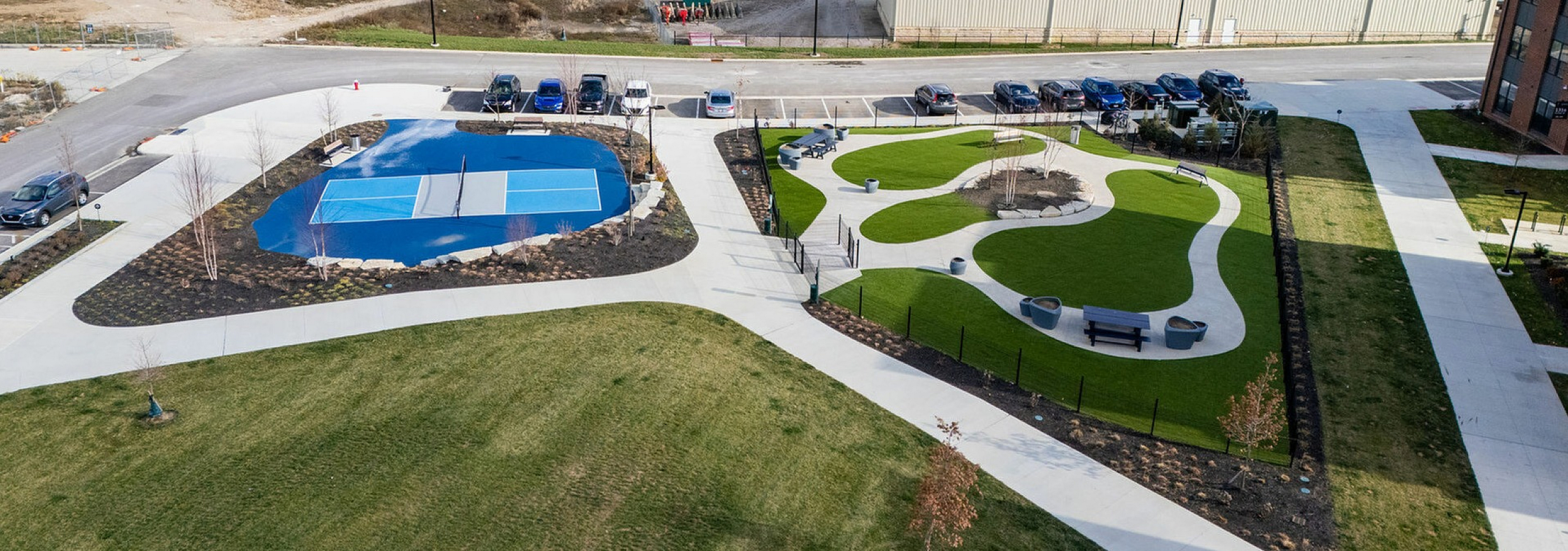 Aerial view of modern urban park with tennis court, landscaped gardens, and surrounding city skyline.
