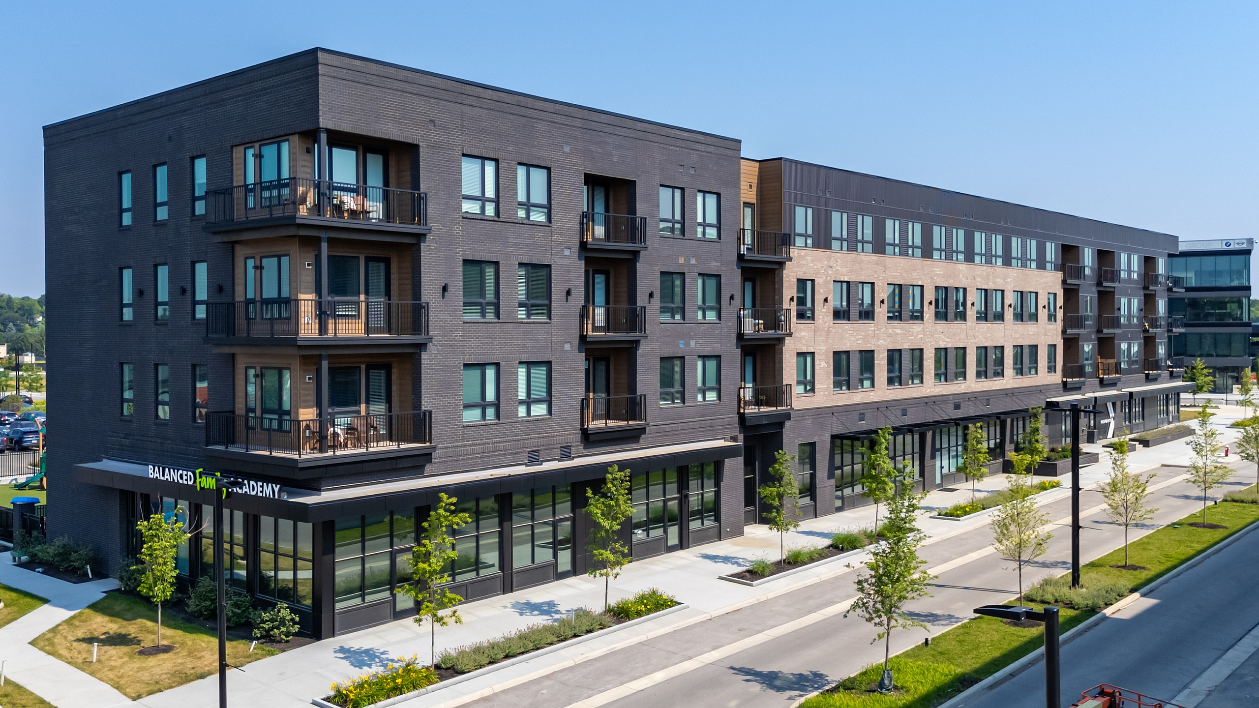 Modern multi-story apartment building with balconies and landscaped surroundings in a bustling urban area.