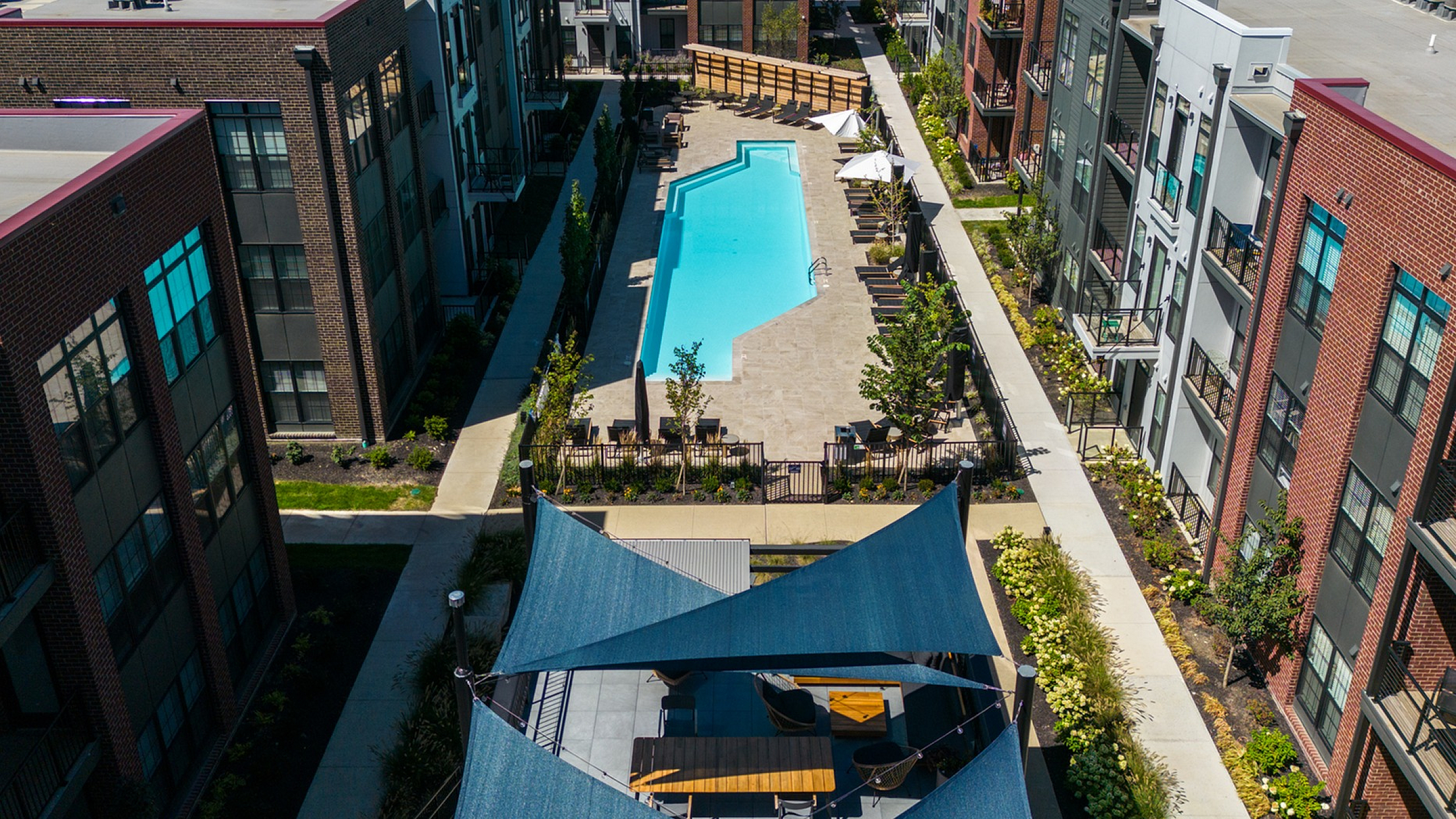 Aerial view of a modern apartment complex with a central swimming pool and surrounding landscaping.
