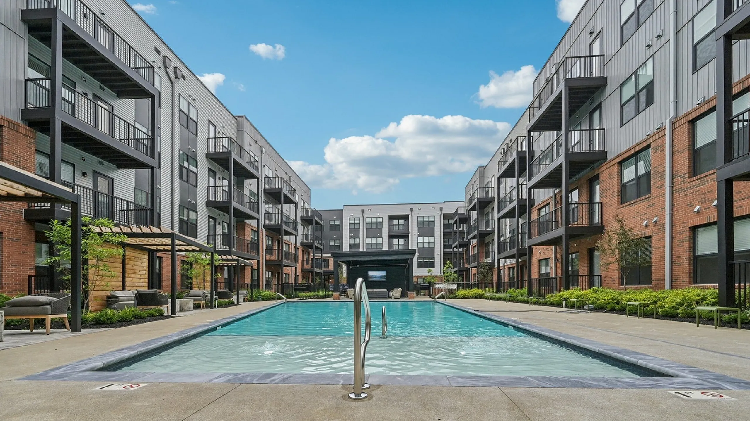 Modern apartment complex with a luxurious central swimming pool, surrounded by stylish balconies and a beautiful sparkling pool with cabanas under a bright blue sky.