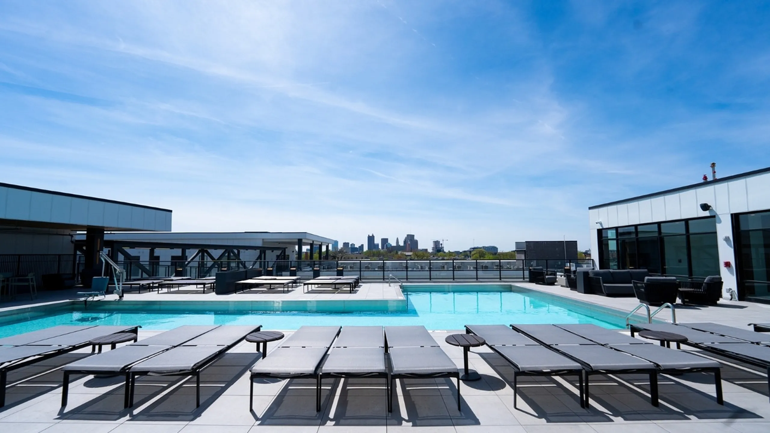 Chic rooftop pool area with panoramic city skyline views, featuring modern lounge chairs and sleek design.