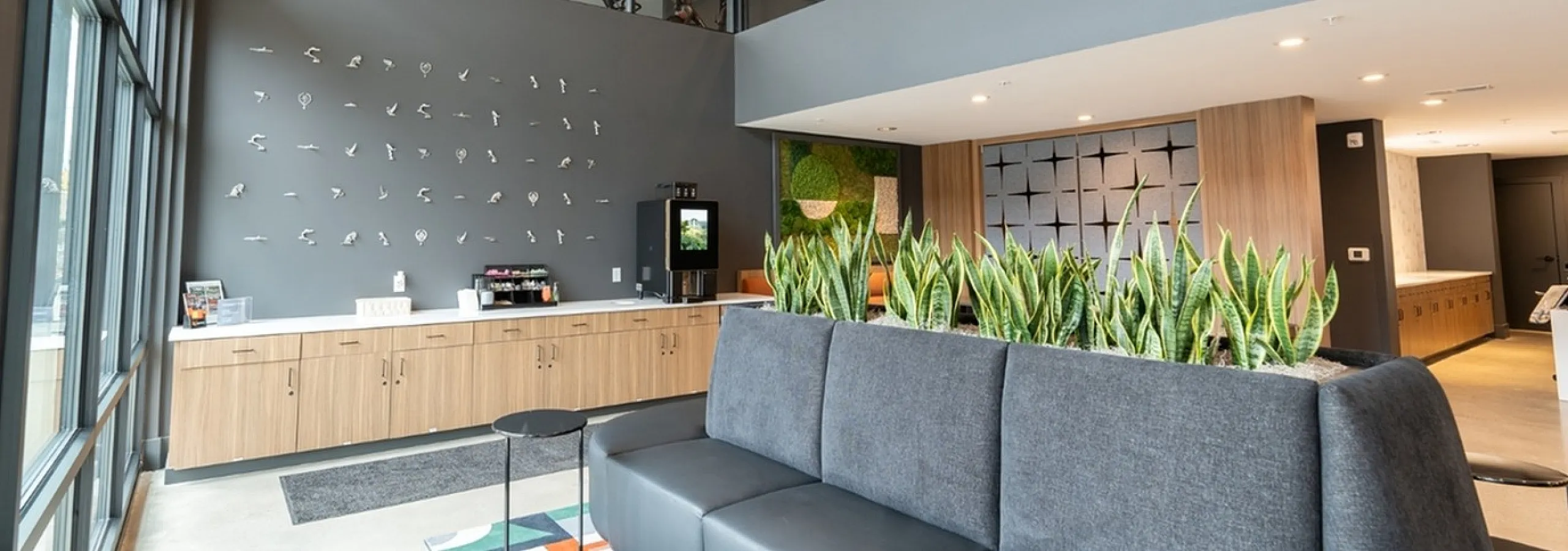 Modern lobby with high ceilings, stylish decor, and abundant natural light, featuring a plush seating area and vibrant indoor plants.