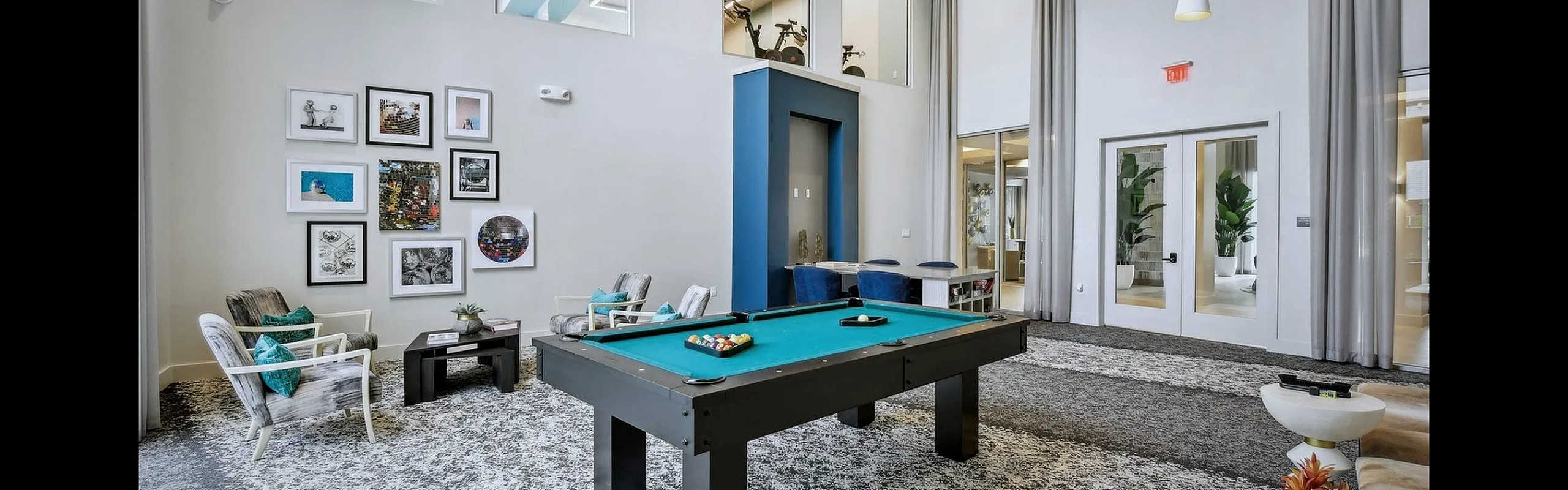 Modern recreation room with a pool table, stylish seating, large windows, and contemporary wall art, creating a vibrant and inviting atmosphere.