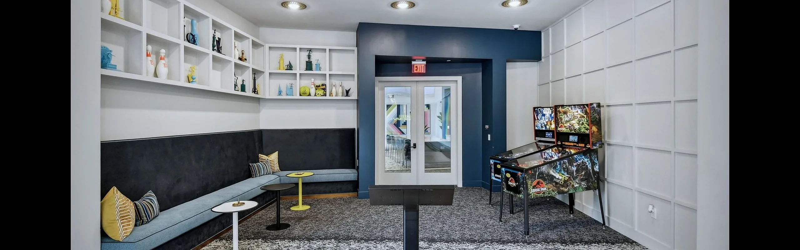 Vibrant recreation room featuring a cozy sectional sofa, colorful bowling balls, a pinball machine, and creative shelving decor.