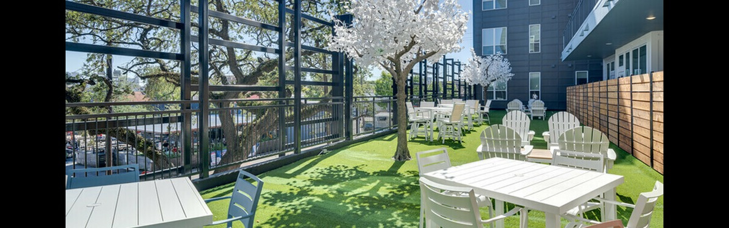 Chic outdoor terrace with modern seating, vibrant greenery, and decorative trees, perfect for relaxation or entertaining in a contemporary apartment complex.