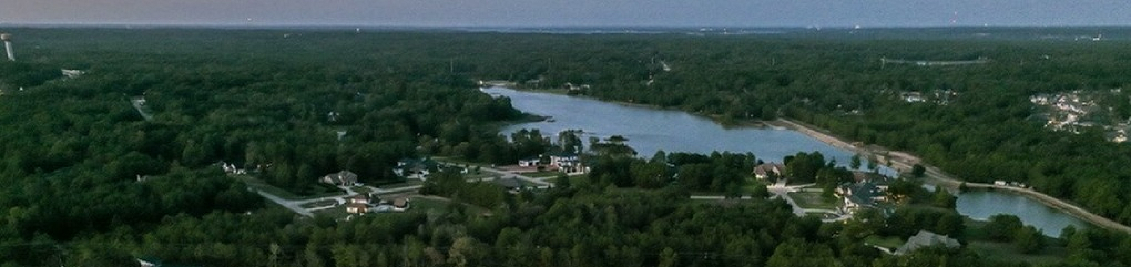 Stunning aerial view of modern apartment complex surrounded by lush greenery and a serene lake, offering a peaceful and picturesque living environment.