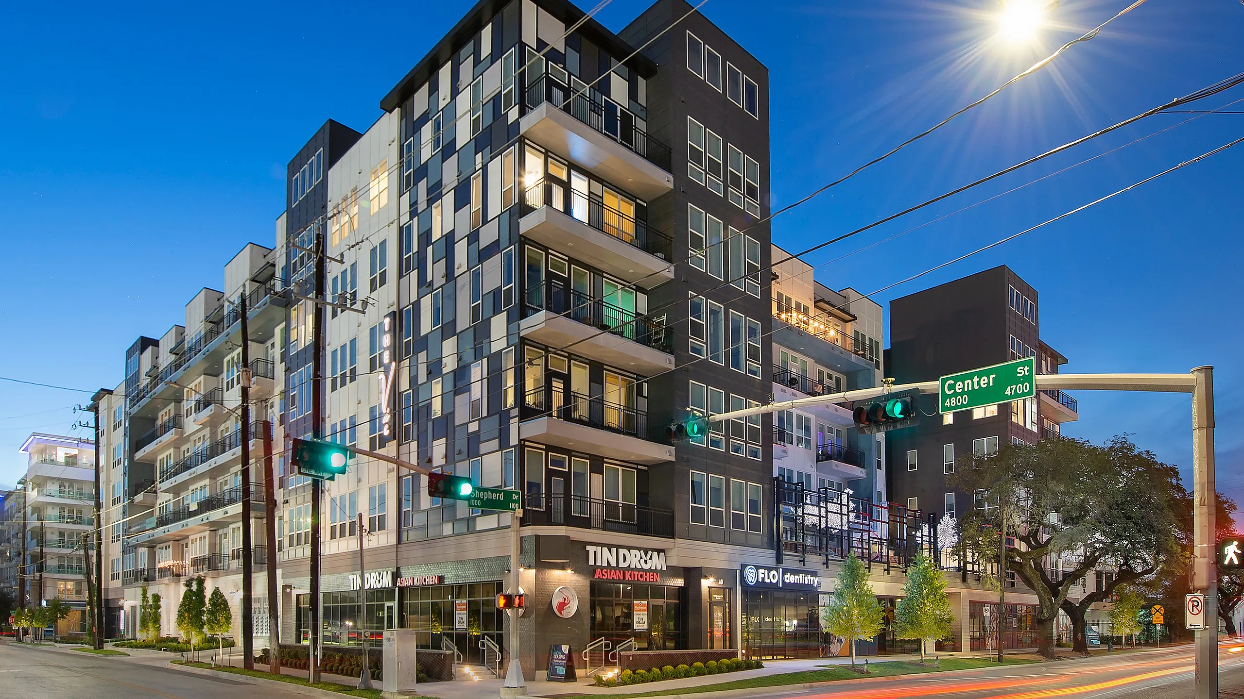 Modern urban apartment building with sleek glass balconies and vibrant street view at dusk.