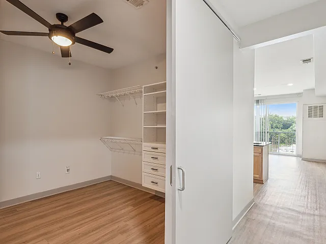 Bright and airy apartment interior featuring a sleek closet with modern shelving, a stylish ceiling fan, and an inviting hallway leading to a balcony with stunning views.