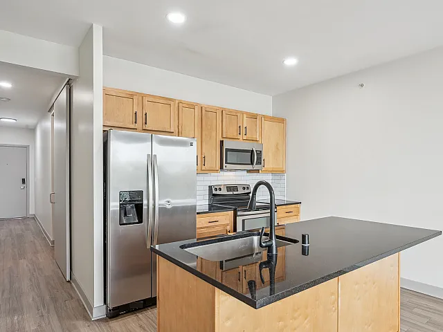 Contemporary kitchen featuring sleek wood cabinets, a shiny stainless steel fridge, and a stylish black countertop with an integrated sink.