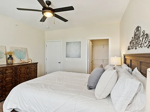 Bright and inviting bedroom featuring a cozy bed with plush pillows, elegant wooden dresser, stylish art, and spacious walk-in closet.