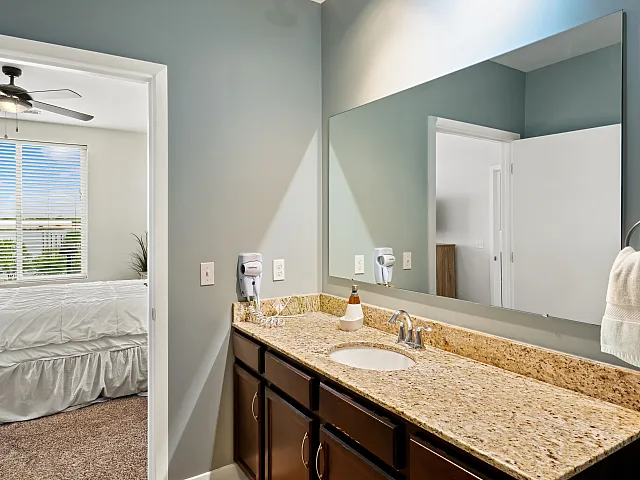 Bright and inviting bathroom featuring a sleek granite countertop and large mirror, with a glimpse into the cozy adjacent bedroom.