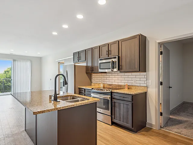 Modern kitchen with granite countertops and stainless steel appliances, featuring an open layout with natural light streaming in through large windows.