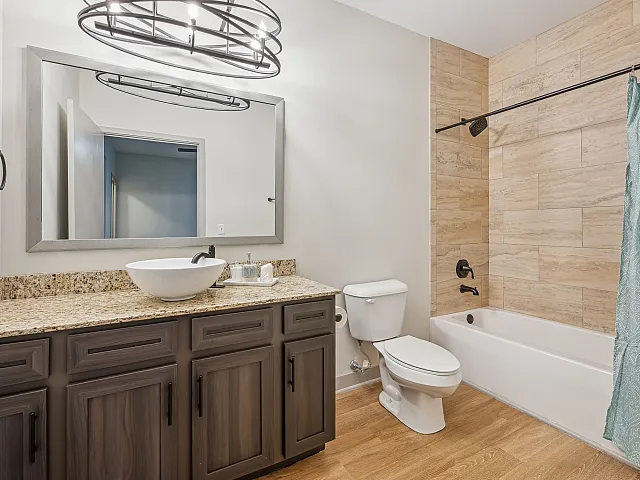 Modern bathroom featuring luxurious granite countertops, elegant vessel sink, and stylish wood cabinetry. Includes a sleek bathtub with contemporary fixtures and a chic blue shower curtain, perfect for relaxation.