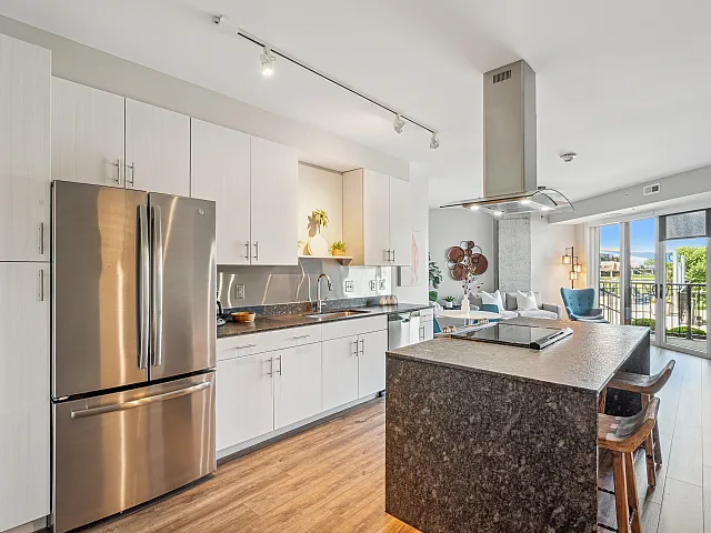 Modern kitchen with sleek stainless steel appliances, chic island, and open living area leading to a bright balcony view.