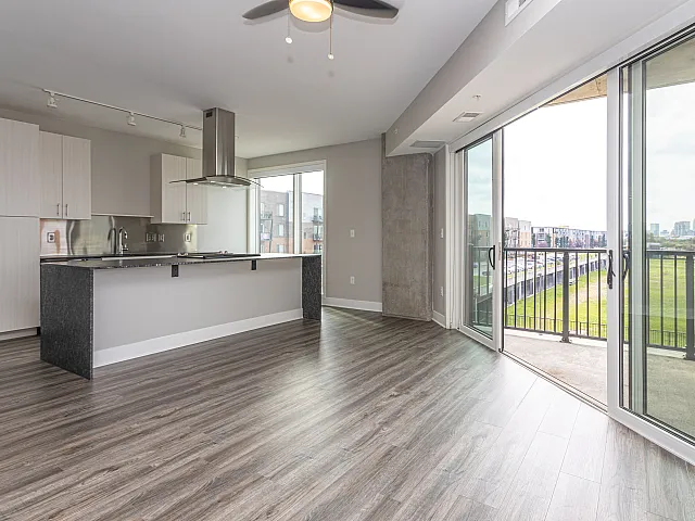 Modern open-concept apartment featuring a sleek kitchen island with granite countertops and stainless steel appliances, leading to a sunlit living area with expansive floor-to-ceiling windows and a private balcony.