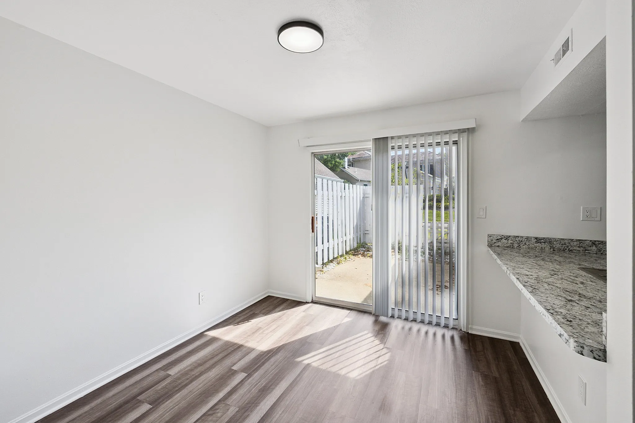 Bright and airy room with modern laminate flooring, sliding glass doors to a private patio, and a sleek granite countertop, perfect for stylish living.