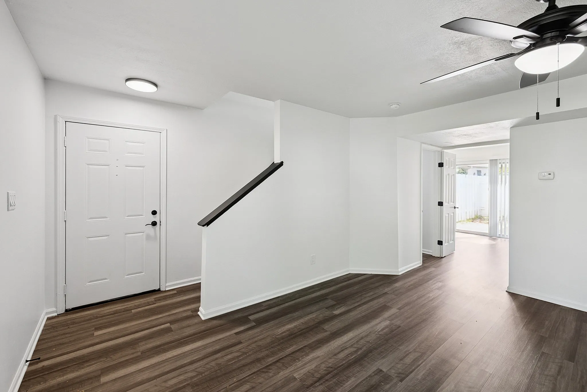 Inviting entryway with elegant dark wood flooring, fresh white walls, and a modern ceiling fan, leading to an open and airy living space with natural light.