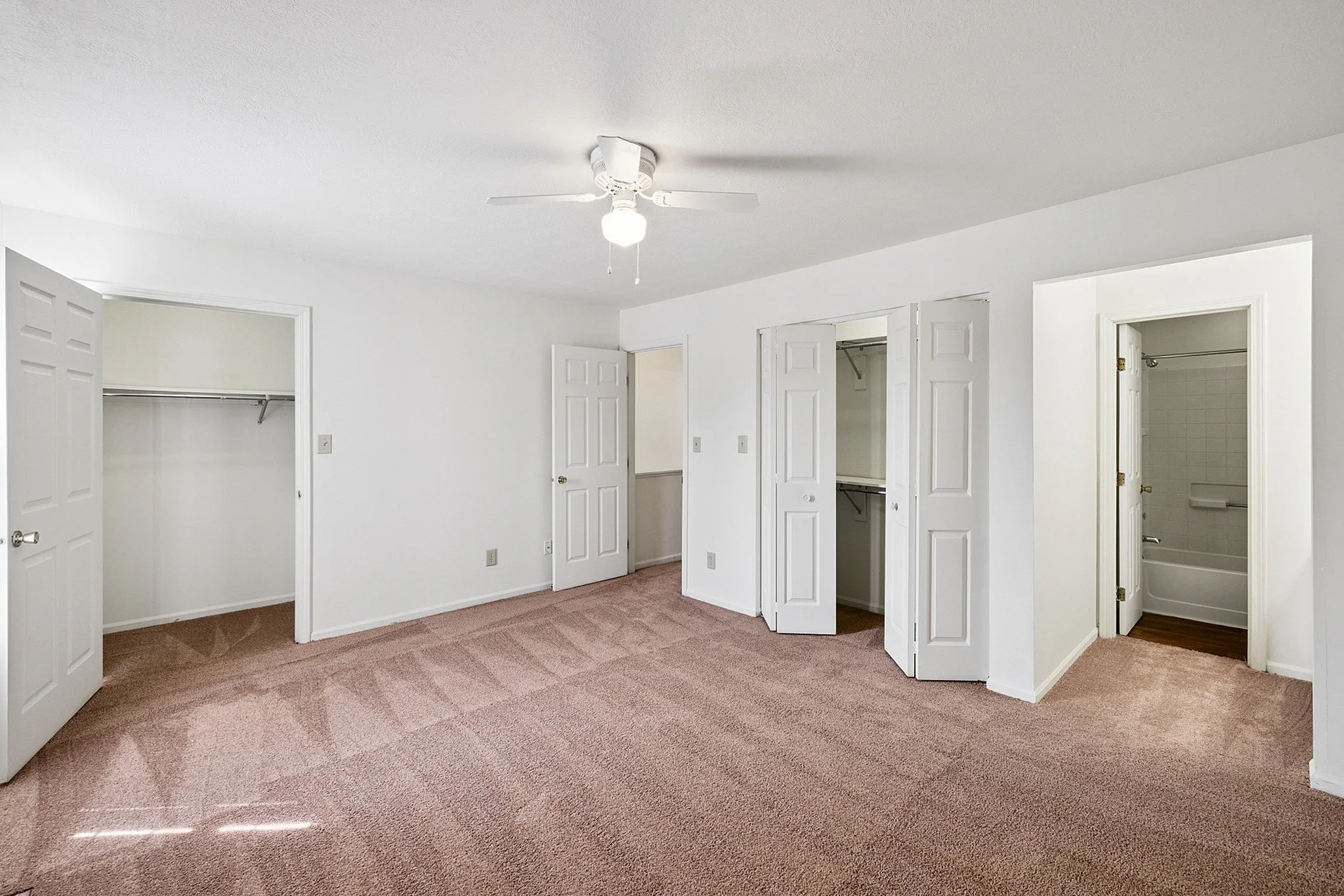Bright and spacious bedroom with plush carpet, generous closet space, and modern ceiling fan.