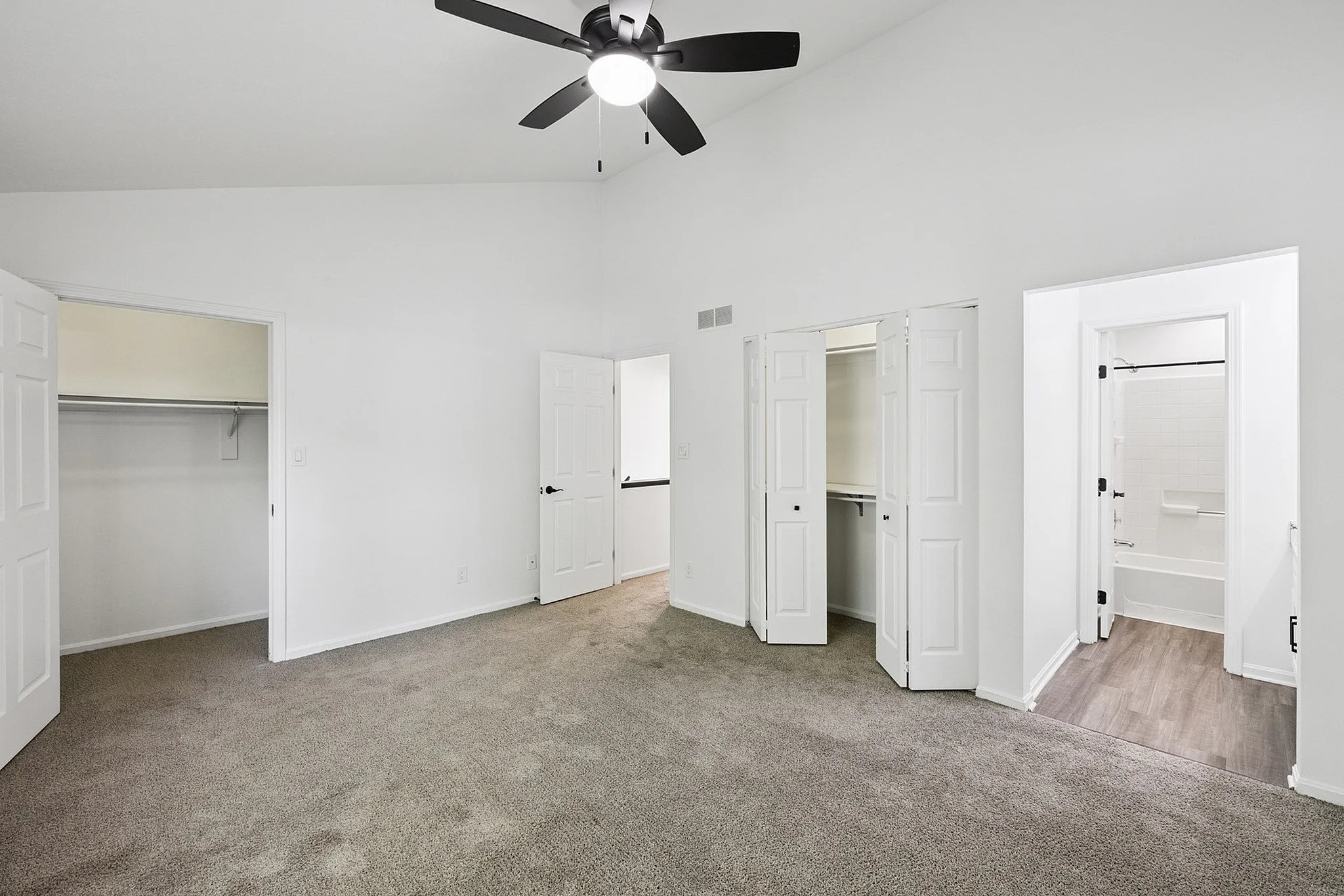 Modern bedroom with plush carpet flooring, elegant ceiling fan, spacious closets, and an adjacent bathroom entrance.