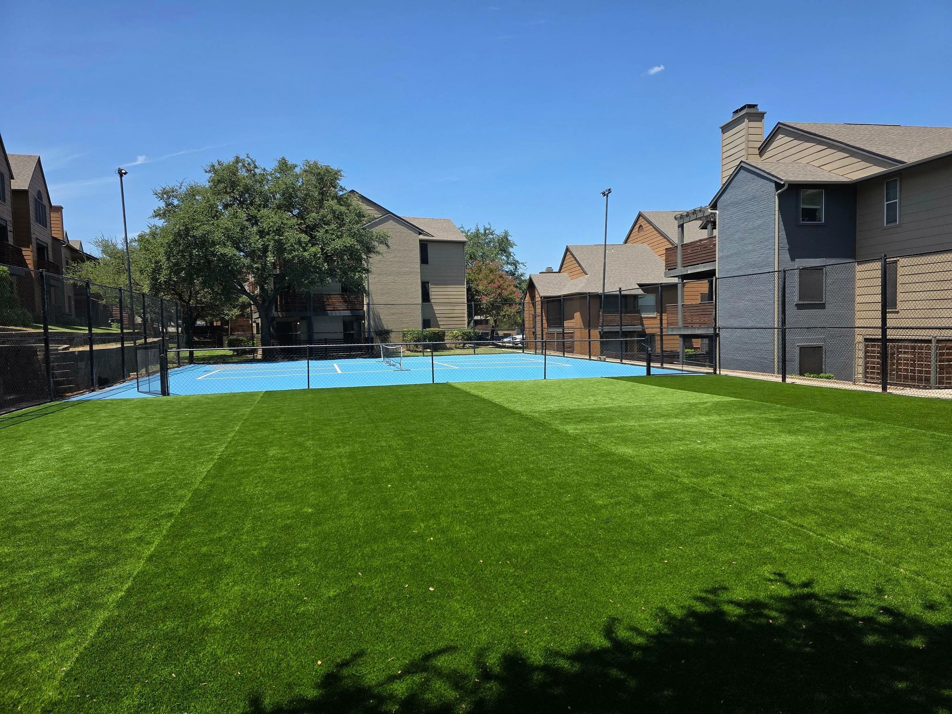 Inviting outdoor tennis court surrounded by lush green landscaping and modern apartment buildings.