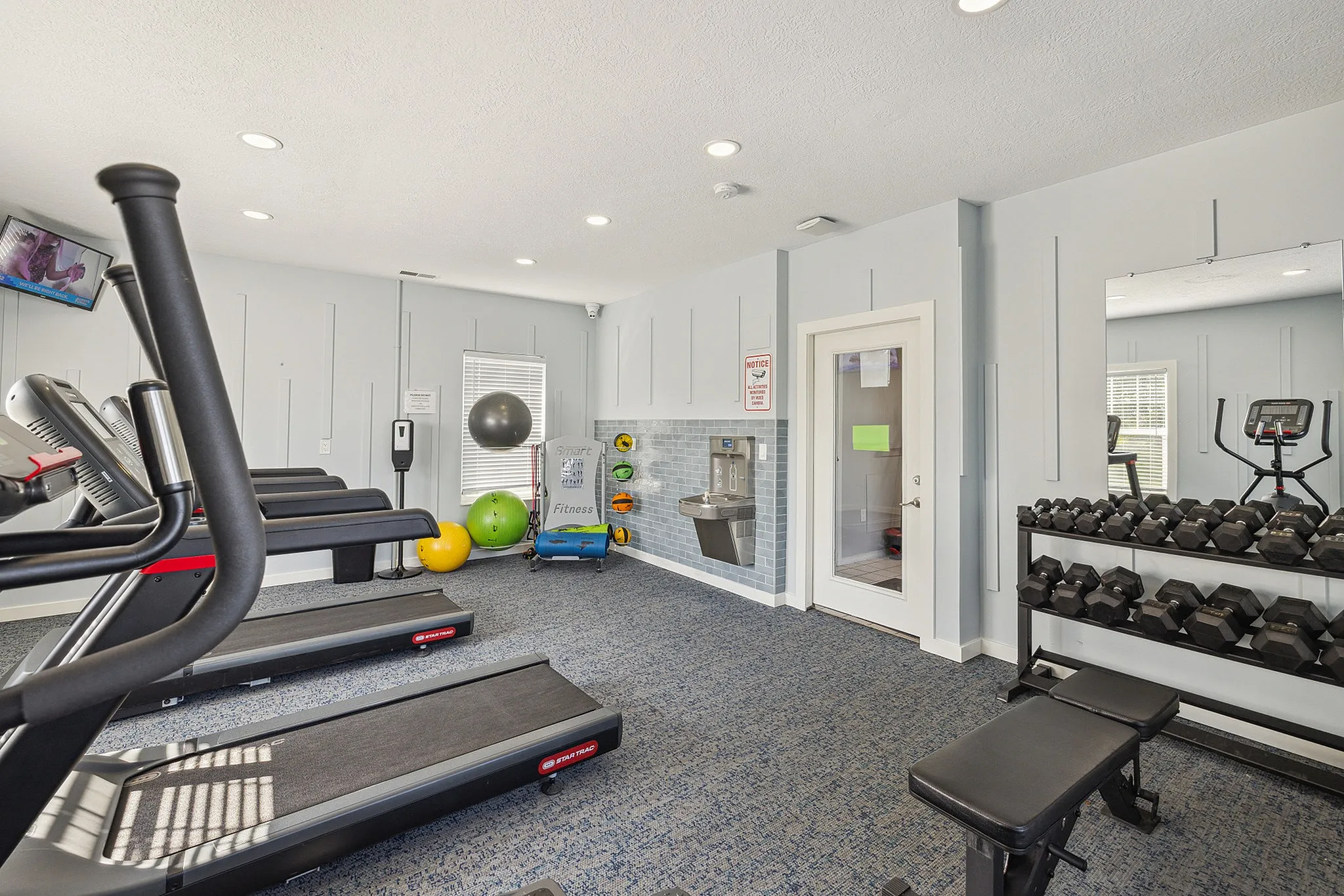 Modern fitness room equipped with treadmills, weights, exercise balls, and ample natural light.