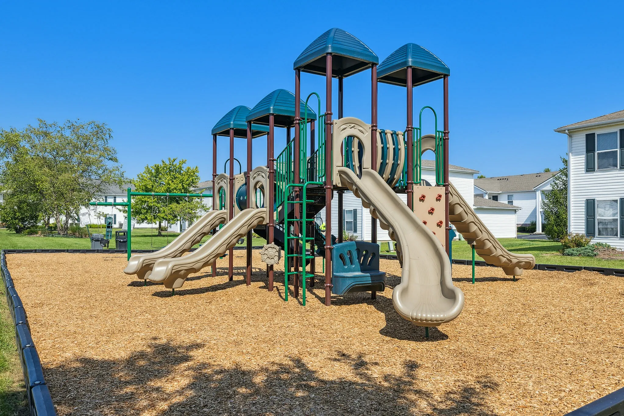 Inviting playground with multiple slides, climbing features, and swings, nestled in a vibrant residential community.