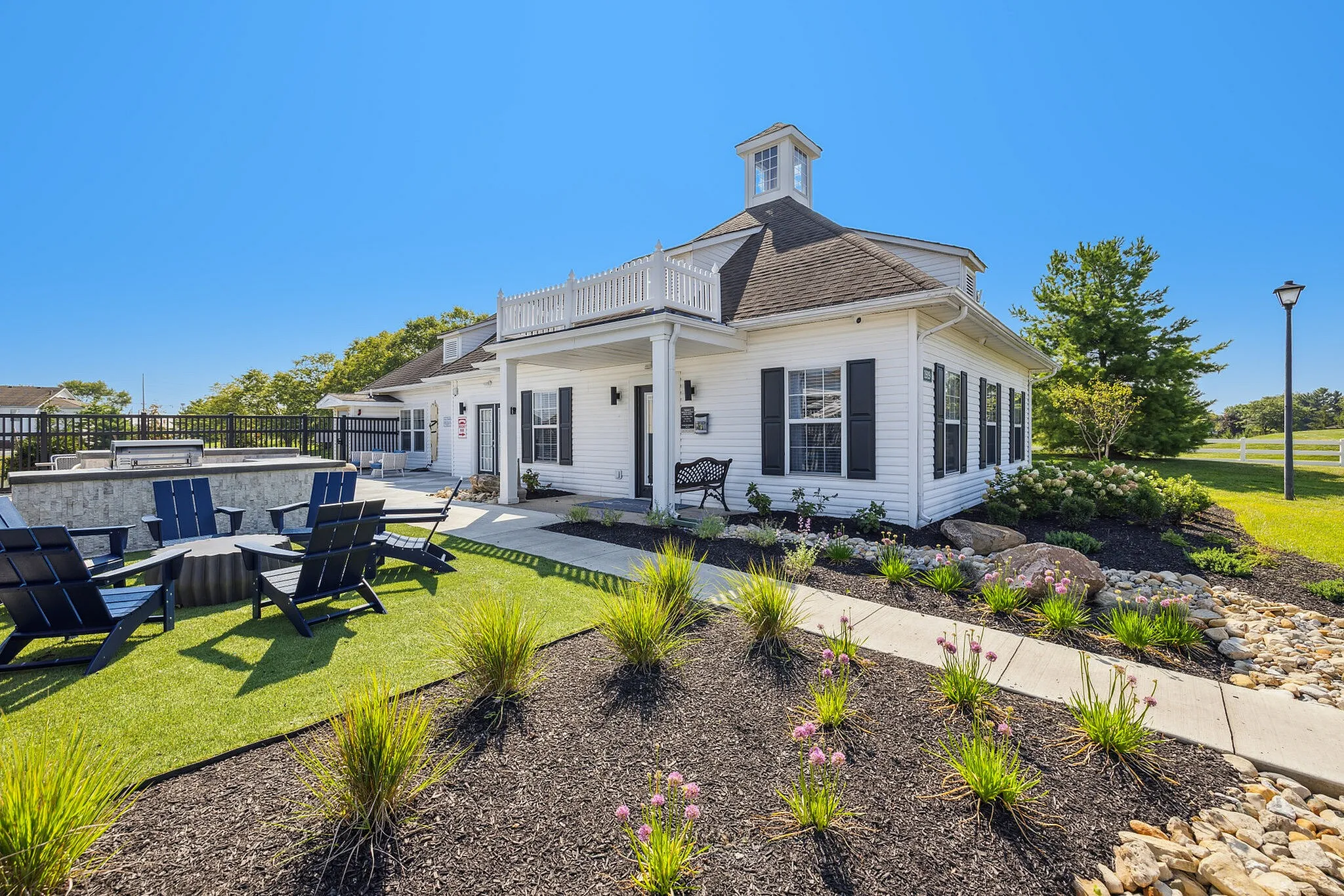 Charming white cottage-style home with a spacious patio, lush landscaping, and inviting outdoor seating under a clear blue sky.