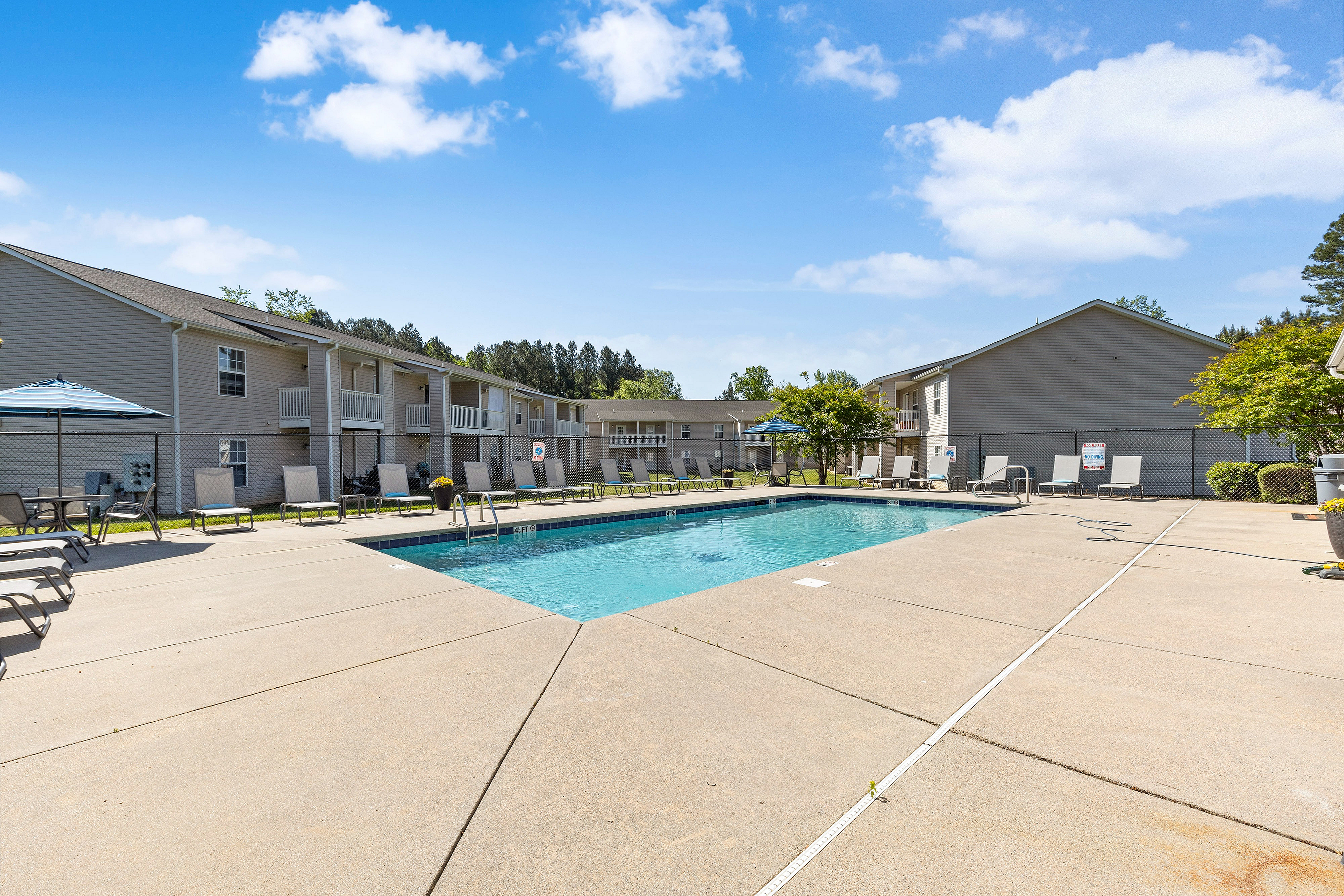 Inviting outdoor apartment pool area with lounge chairs and umbrellas under a bright blue sky, perfect for relaxation and enjoyment.
