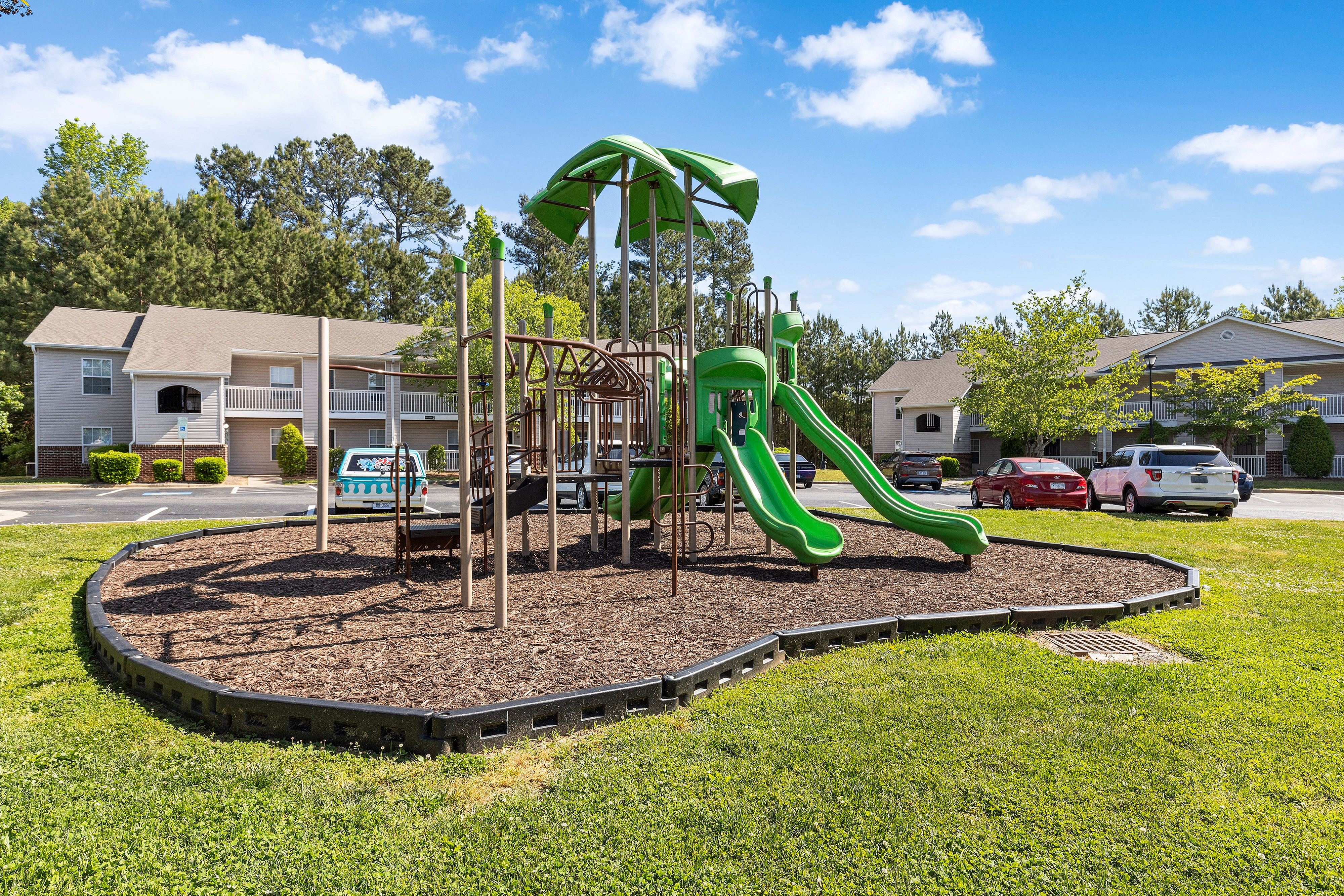 Inviting community playground with vibrant green slides surrounded by lush greenery, ideal for family-friendly living.