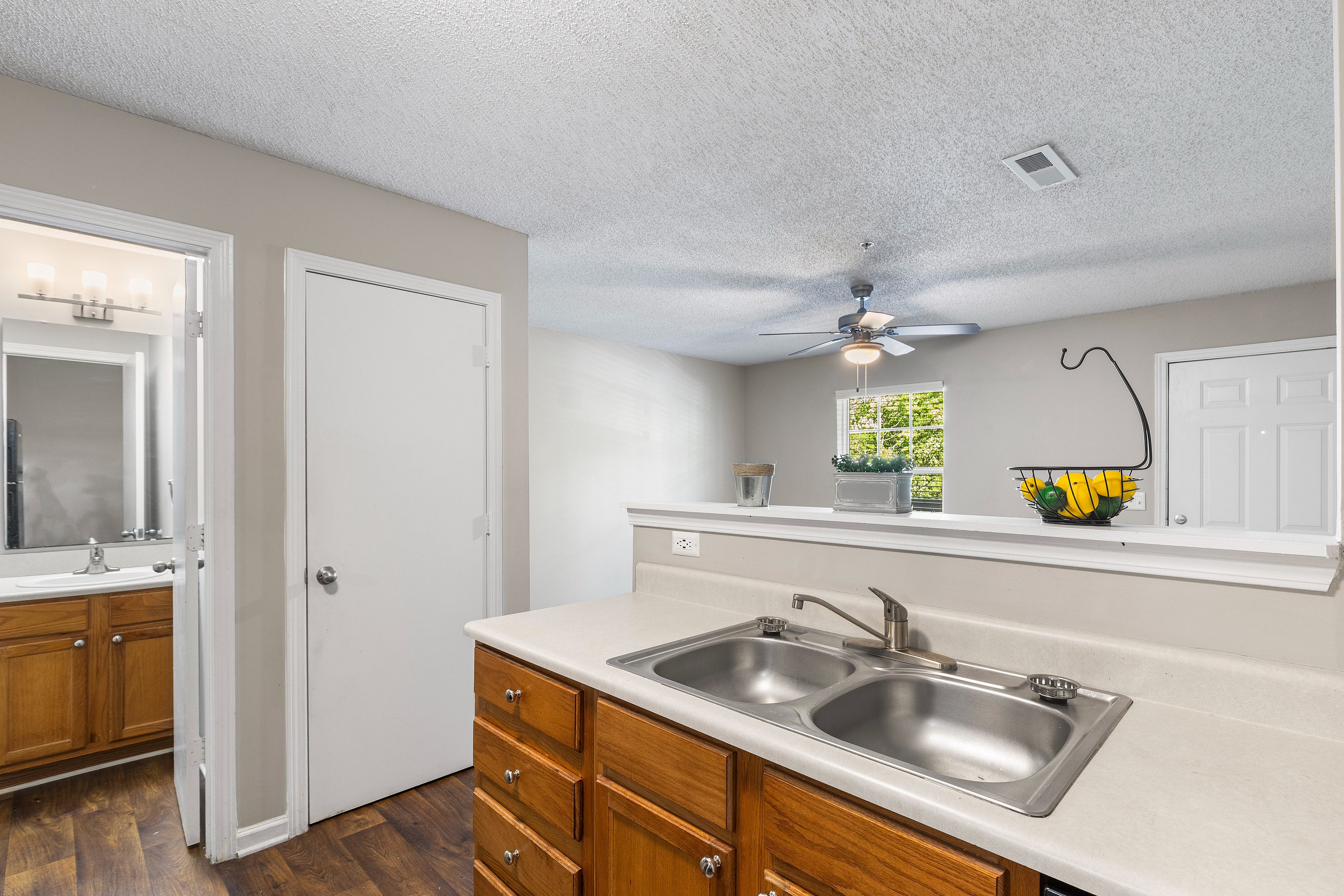 Inviting kitchen with sleek countertops, double sink, and warm wooden cabinetry, leading to a bright, open living space with a modern ceiling fan.