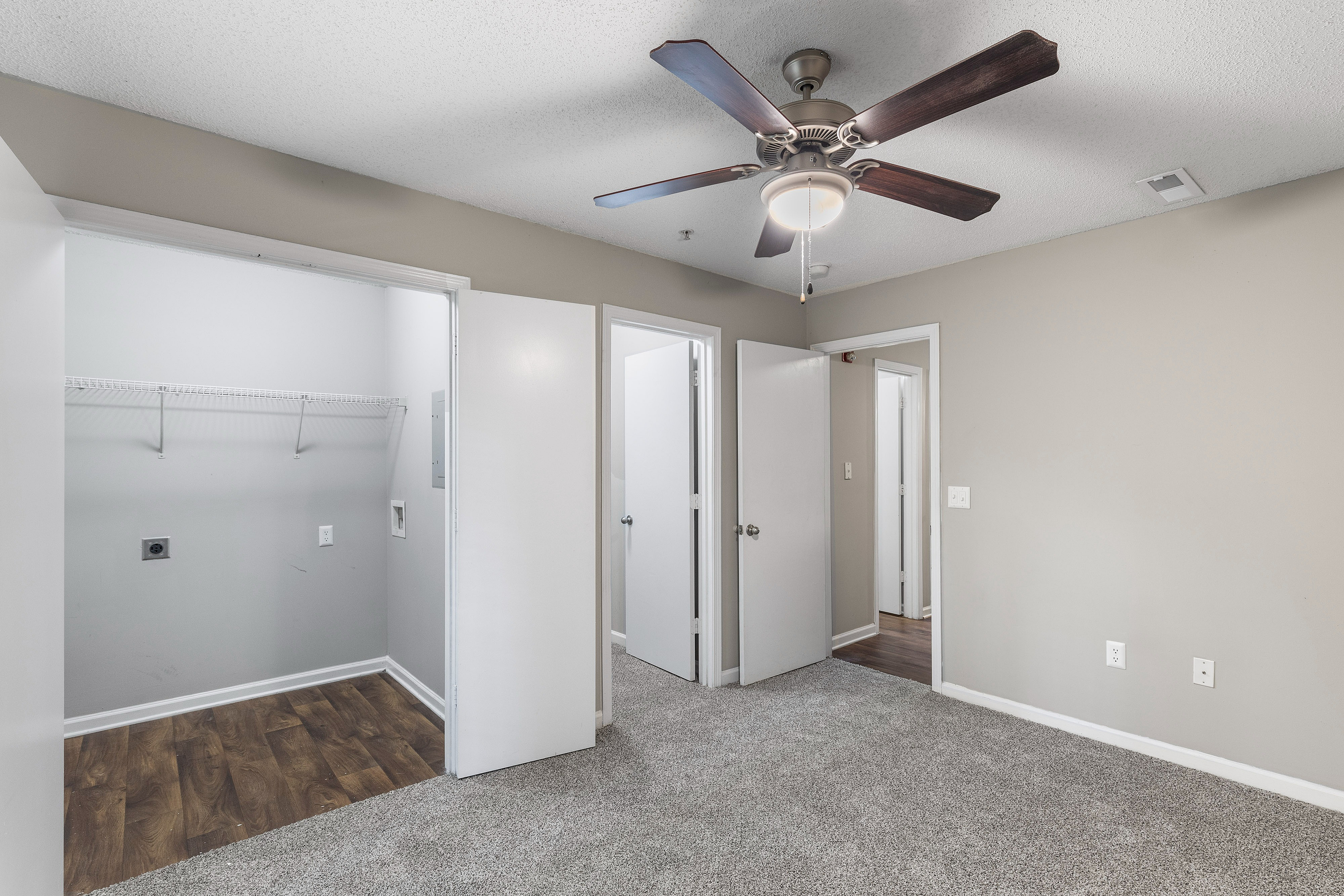 Modern apartment interior showcasing a spacious room with soft carpeting, a ceiling fan, and a versatile closet space, perfect for comfortable living.