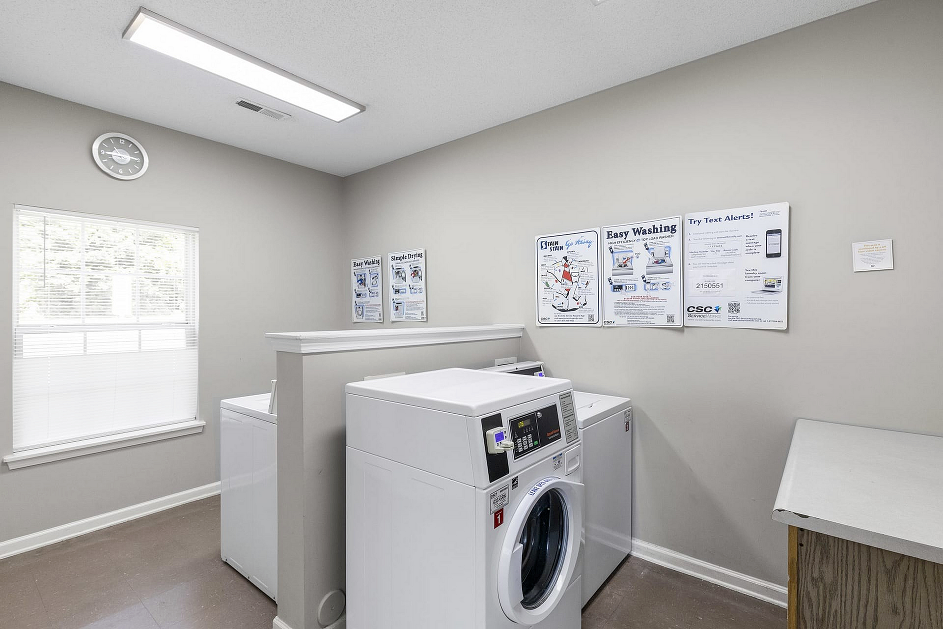 Bright and airy laundry room with modern washing machines, ample light from a large window, and helpful instructional posters.