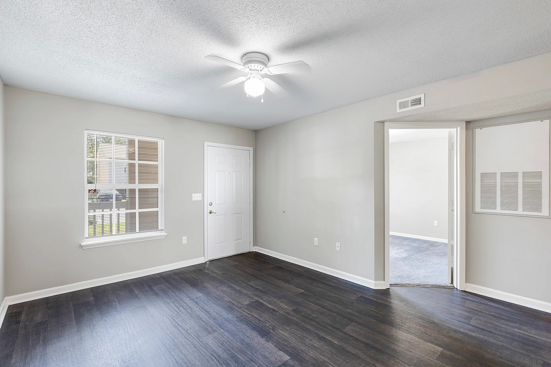 Charming light-filled room with elegant dark wood flooring and modern ceiling fan, boasting a cozy entryway and inviting open layout.