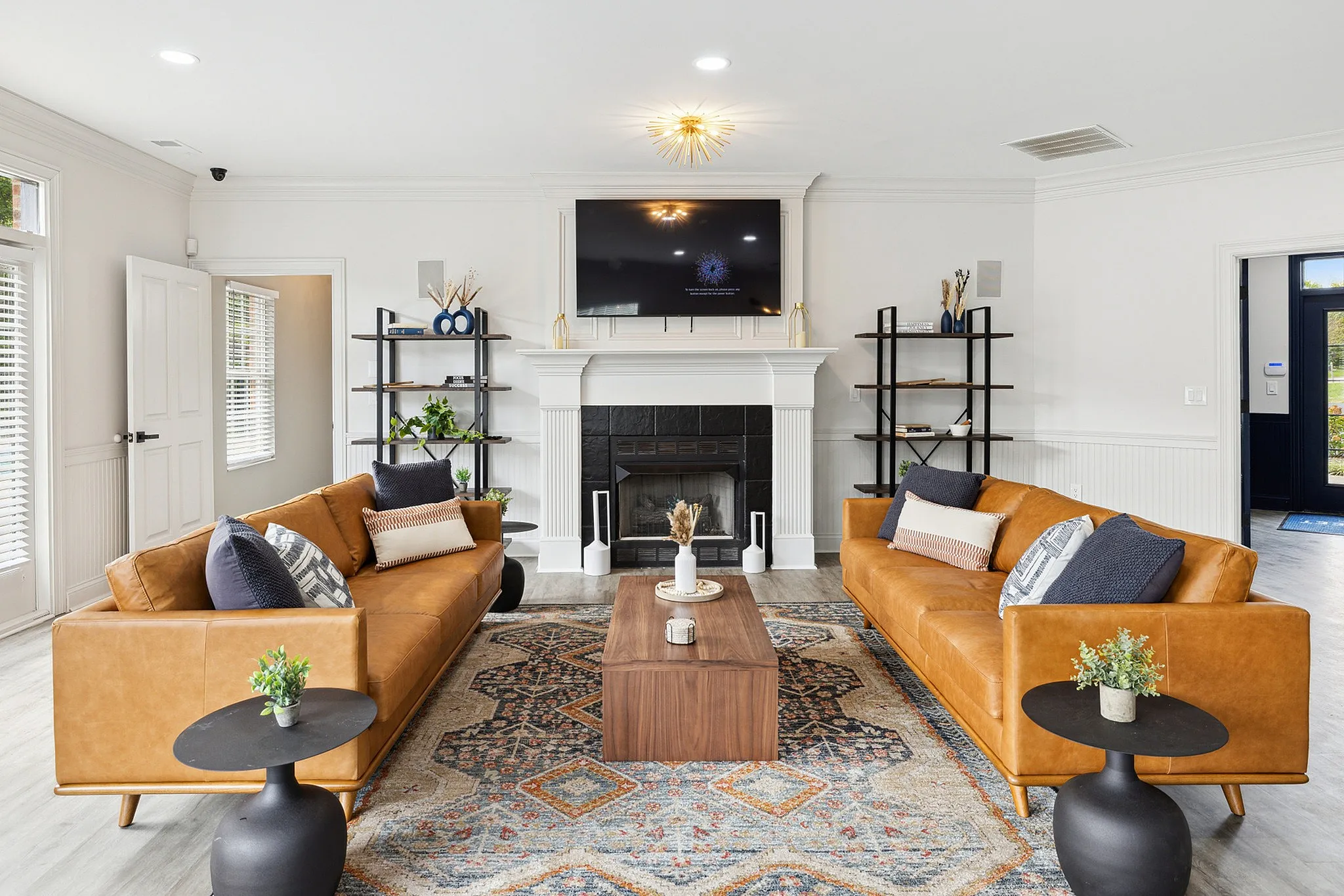 Modern living room featuring elegant leather sofas, chic black tables, and a cozy fireplace, styled with earthy decor and a vibrant area rug.