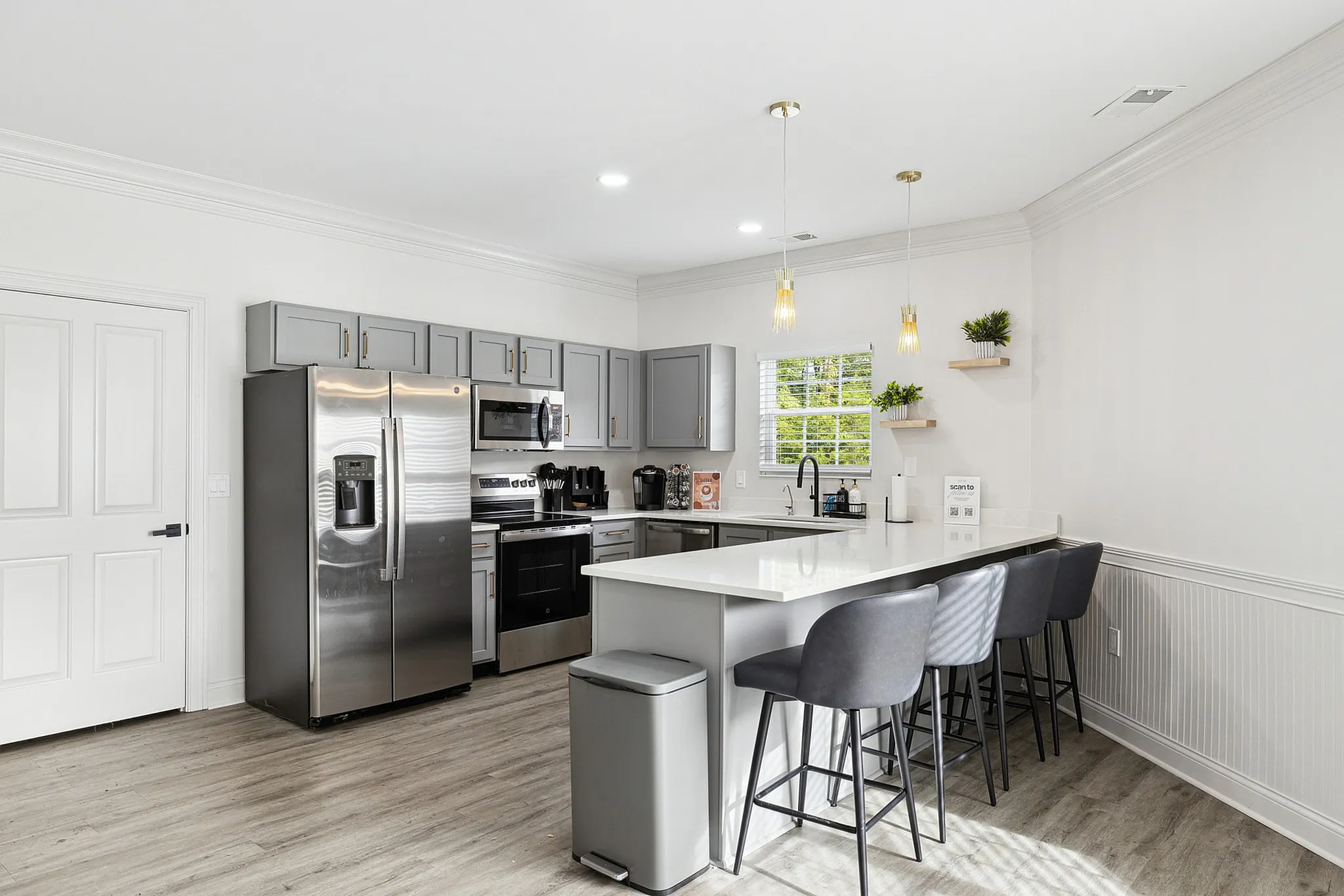 Modern kitchen with sleek stainless steel appliances, elegant gray cabinets, and a stylish breakfast bar with chic pendant lights and seating.