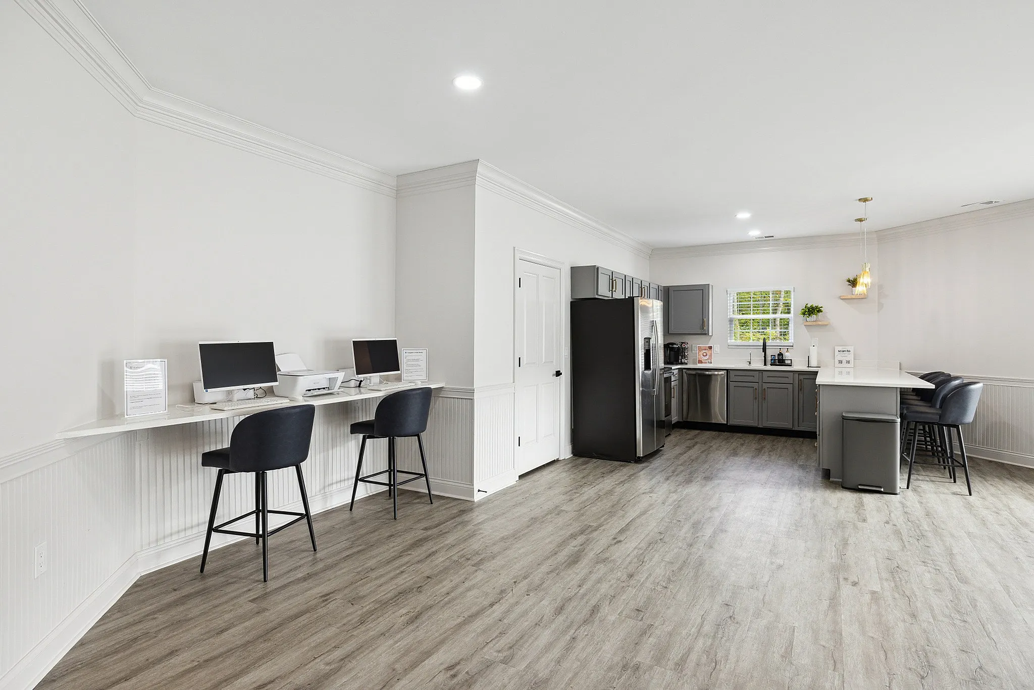 Bright, contemporary shared workspace with sleek kitchen setup, featuring elegant bar stools and state-of-the-art computers.
