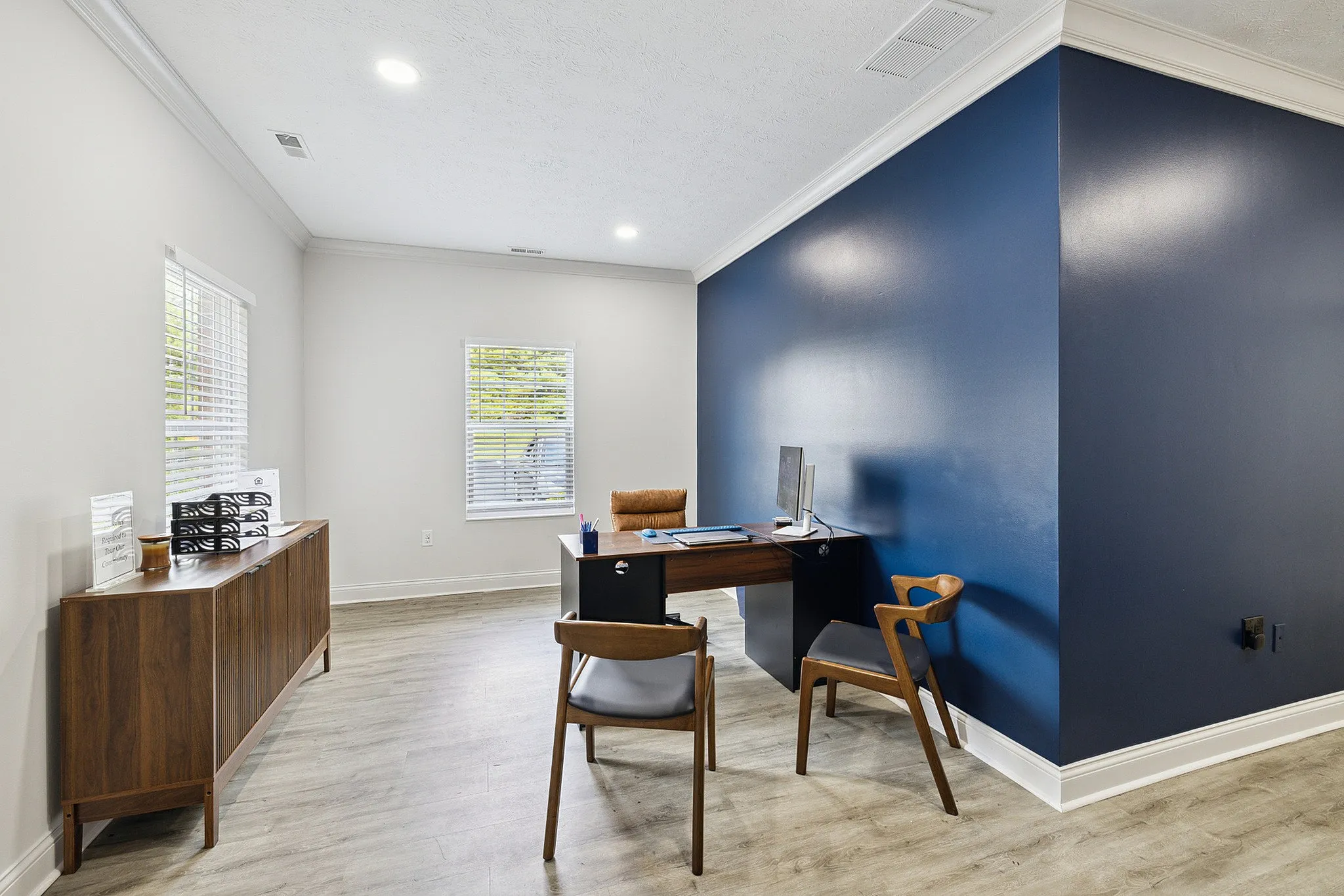 Sophisticated office space with contemporary wooden furniture, accented by a bold blue wall and natural light.