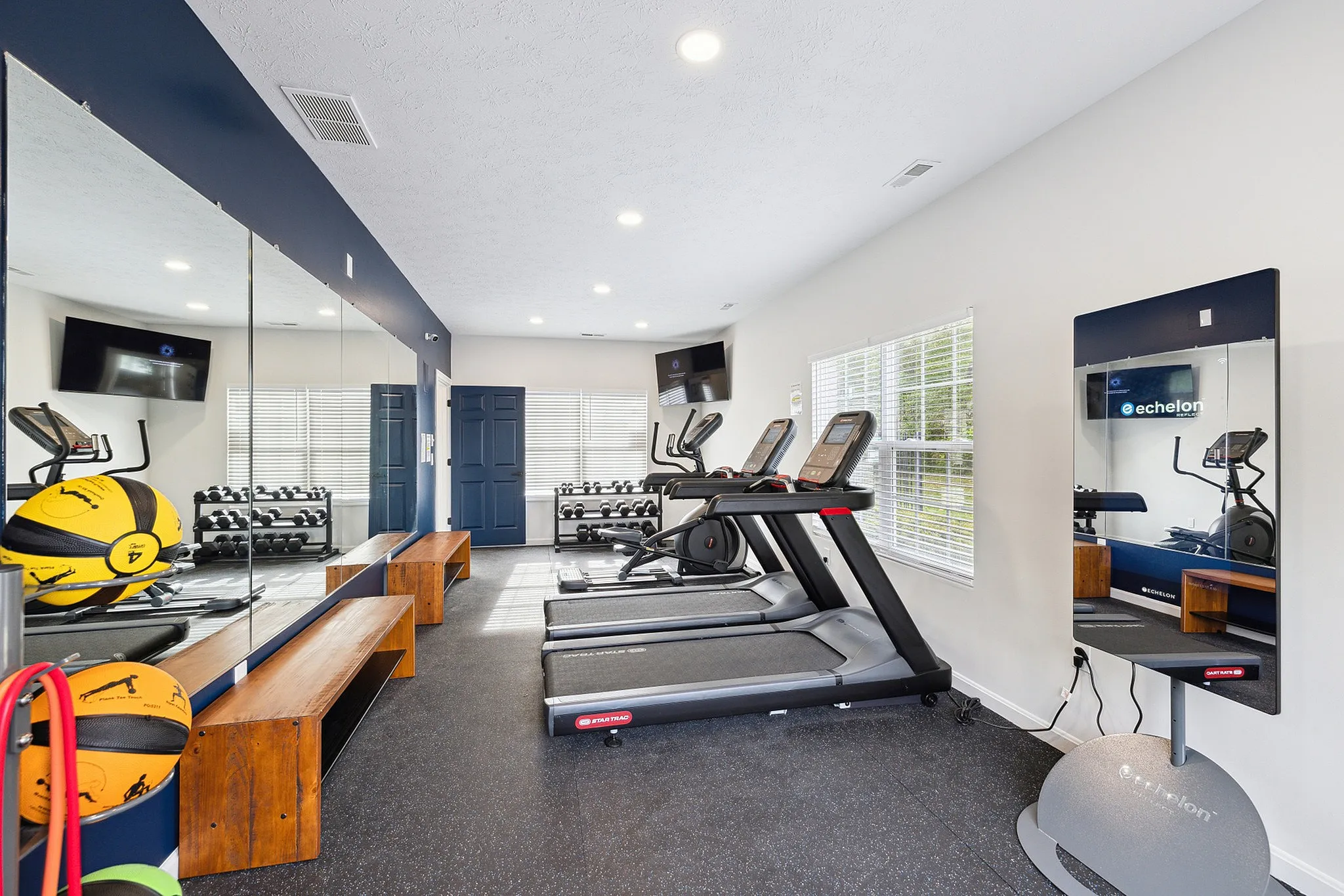 Bright and modern apartment fitness center featuring treadmills, wall mirrors, free weights, and fitness equipment. Ideal for a healthy lifestyle.