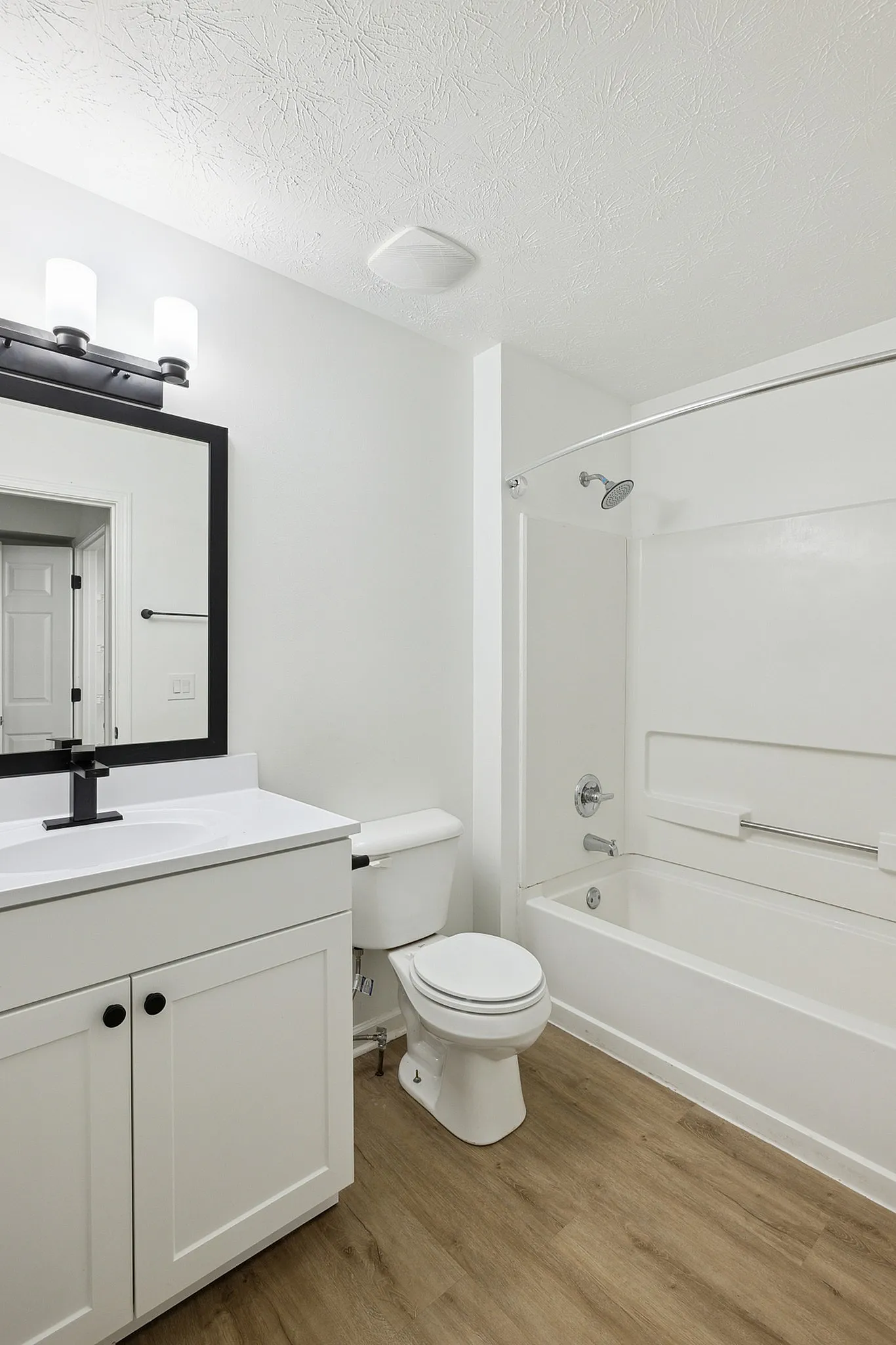 Modern bathroom with sleek white vanity, stylish mirror, and elegant wood flooring.