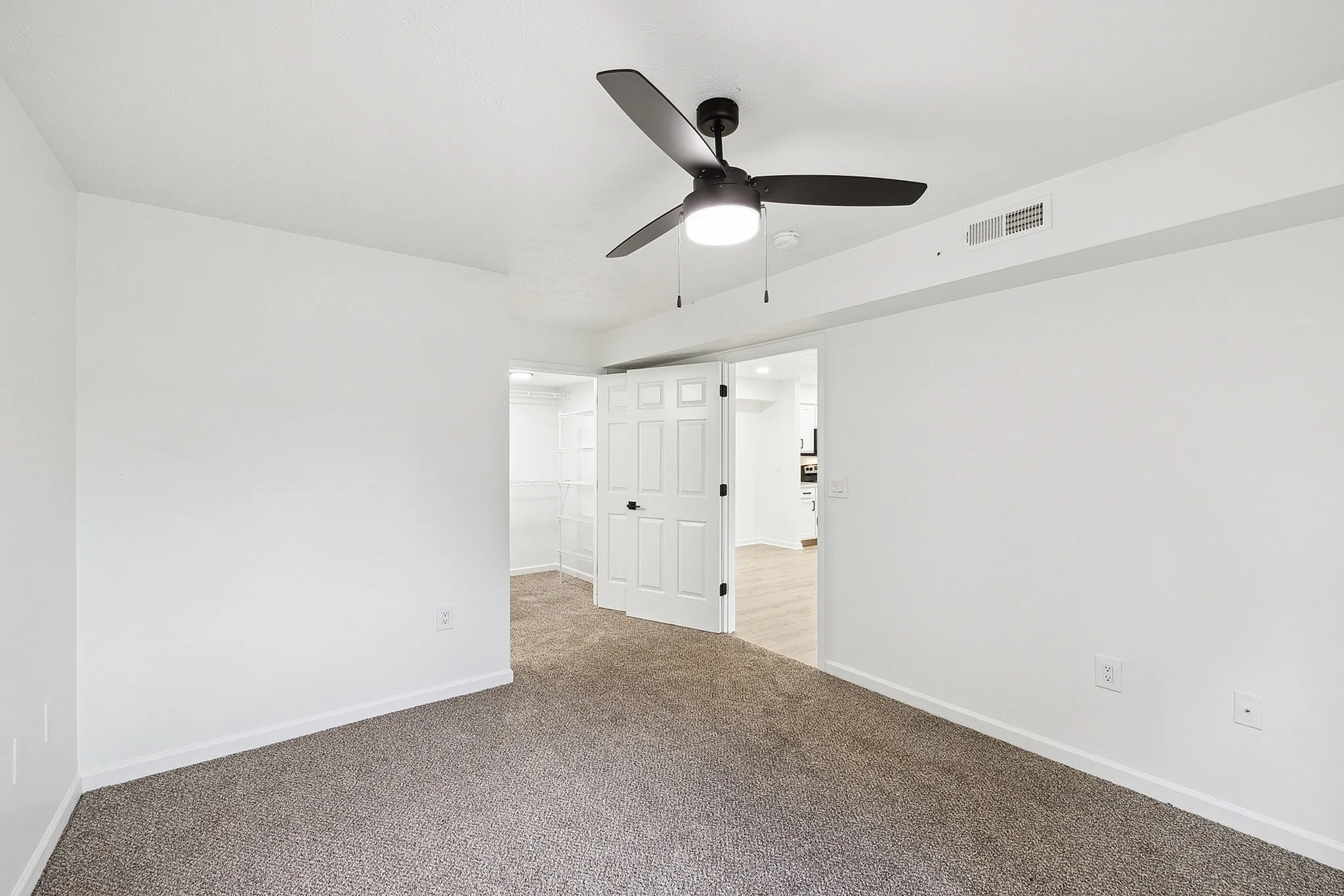 Bright and airy bedroom featuring a modern ceiling fan, plush carpeting, and a walk-in closet with white shelving.