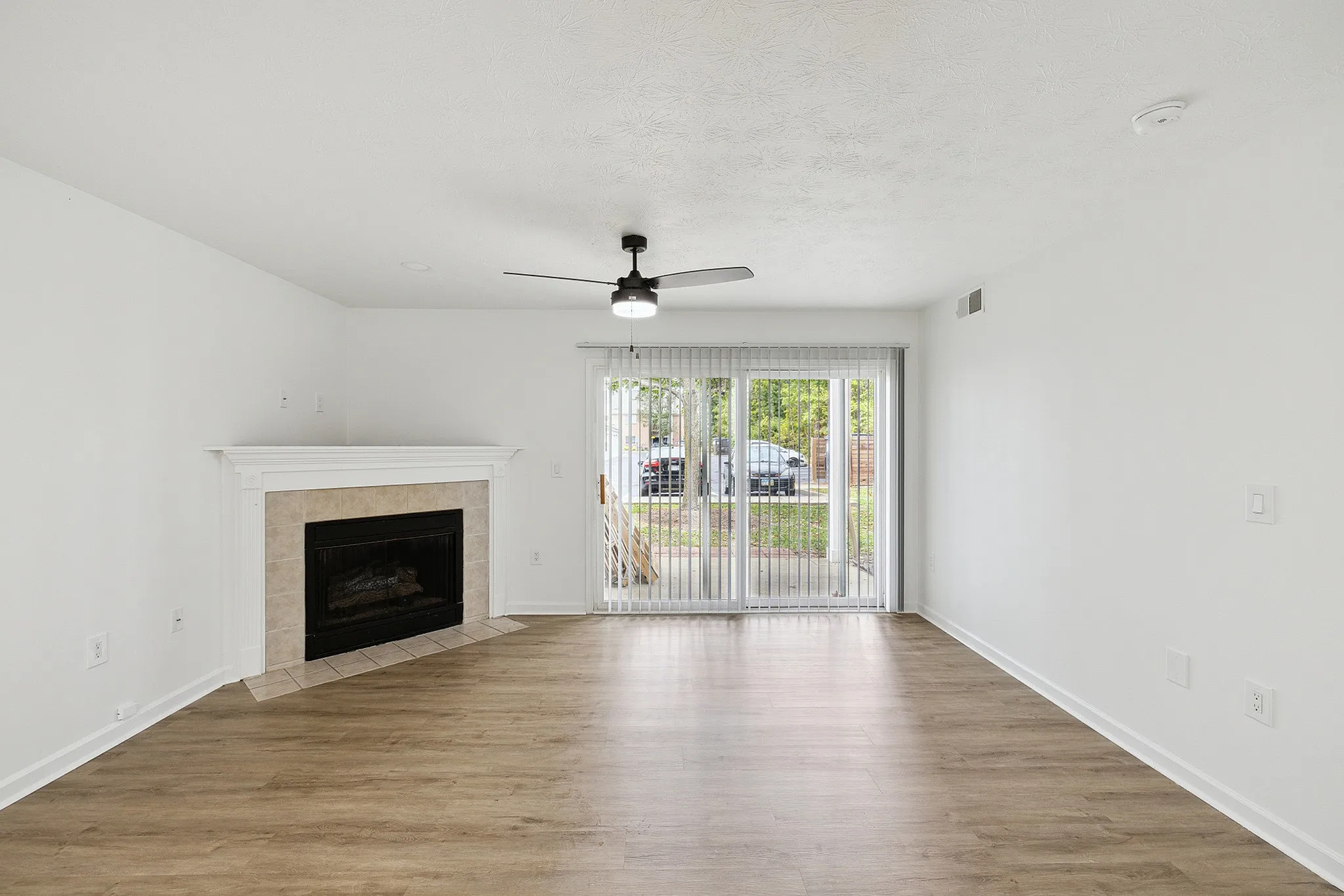 Bright and airy living room with elegant hardwood flooring, a cozy fireplace, and large sliding glass doors leading to a serene outdoor view.