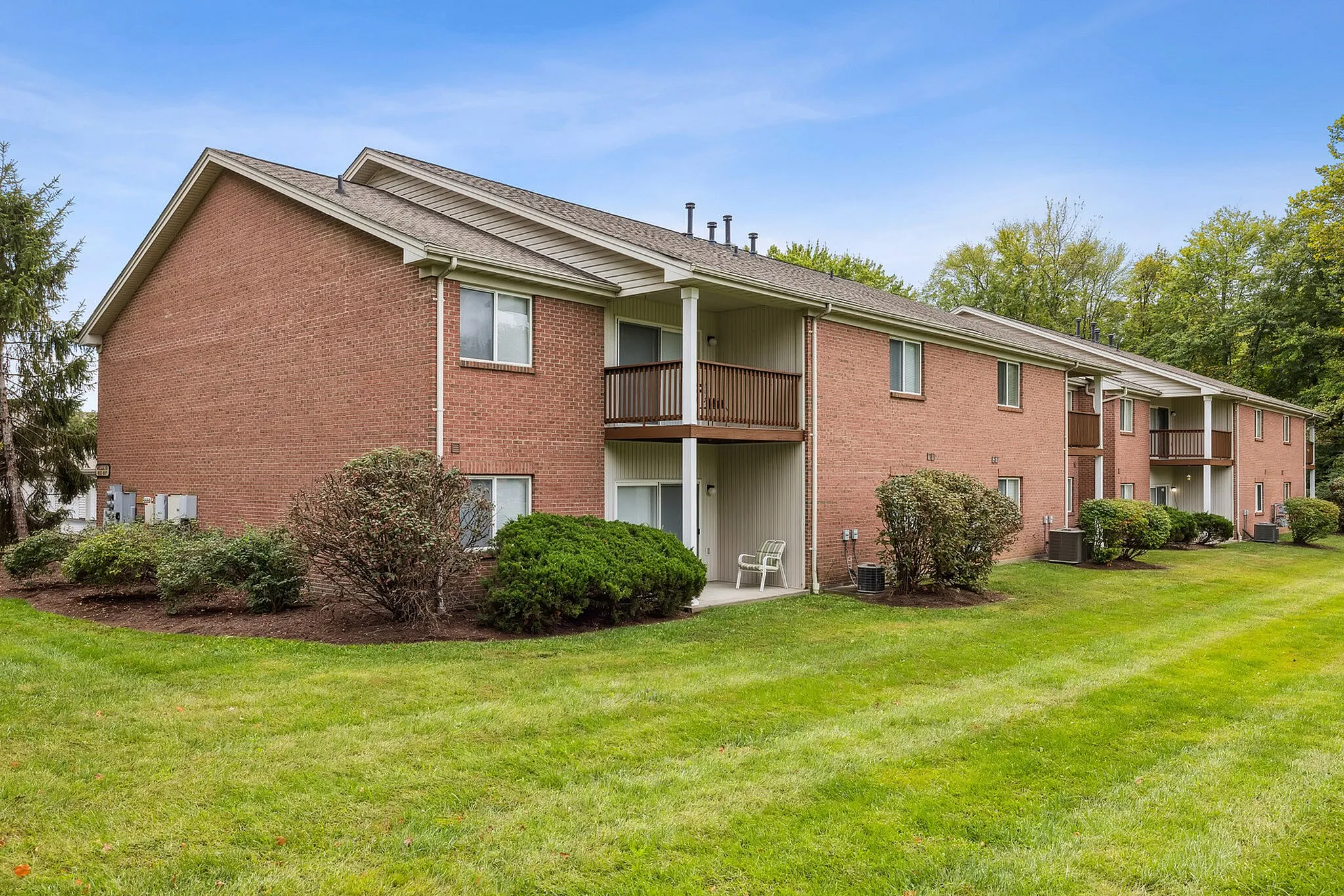 Charming brick apartment complex surrounded by lush greenery and well-manicured lawns, perfect for serene living.