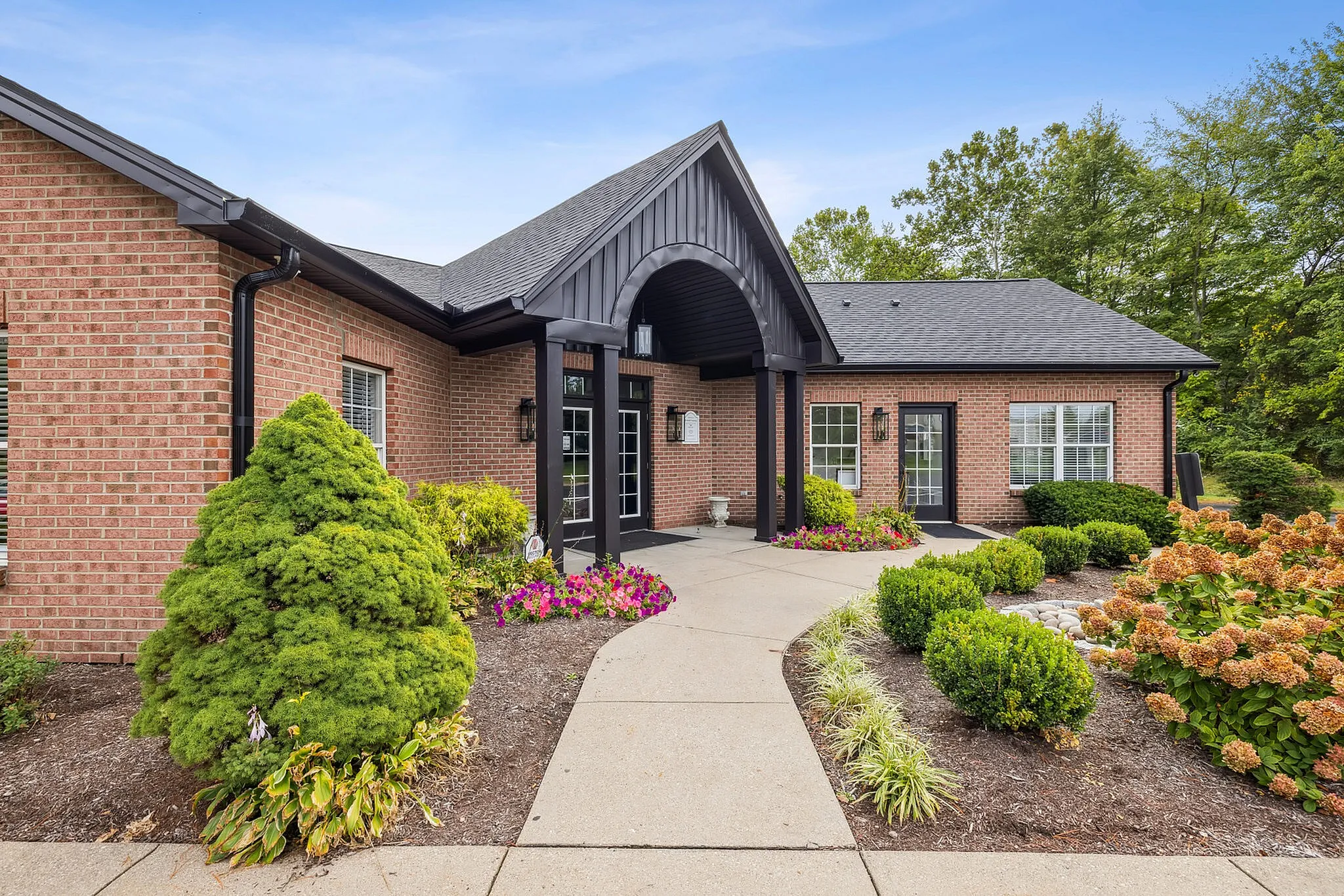 Charming brick apartment building with elegant entrance, surrounded by lush greenery and vibrant flowers in a serene setting.