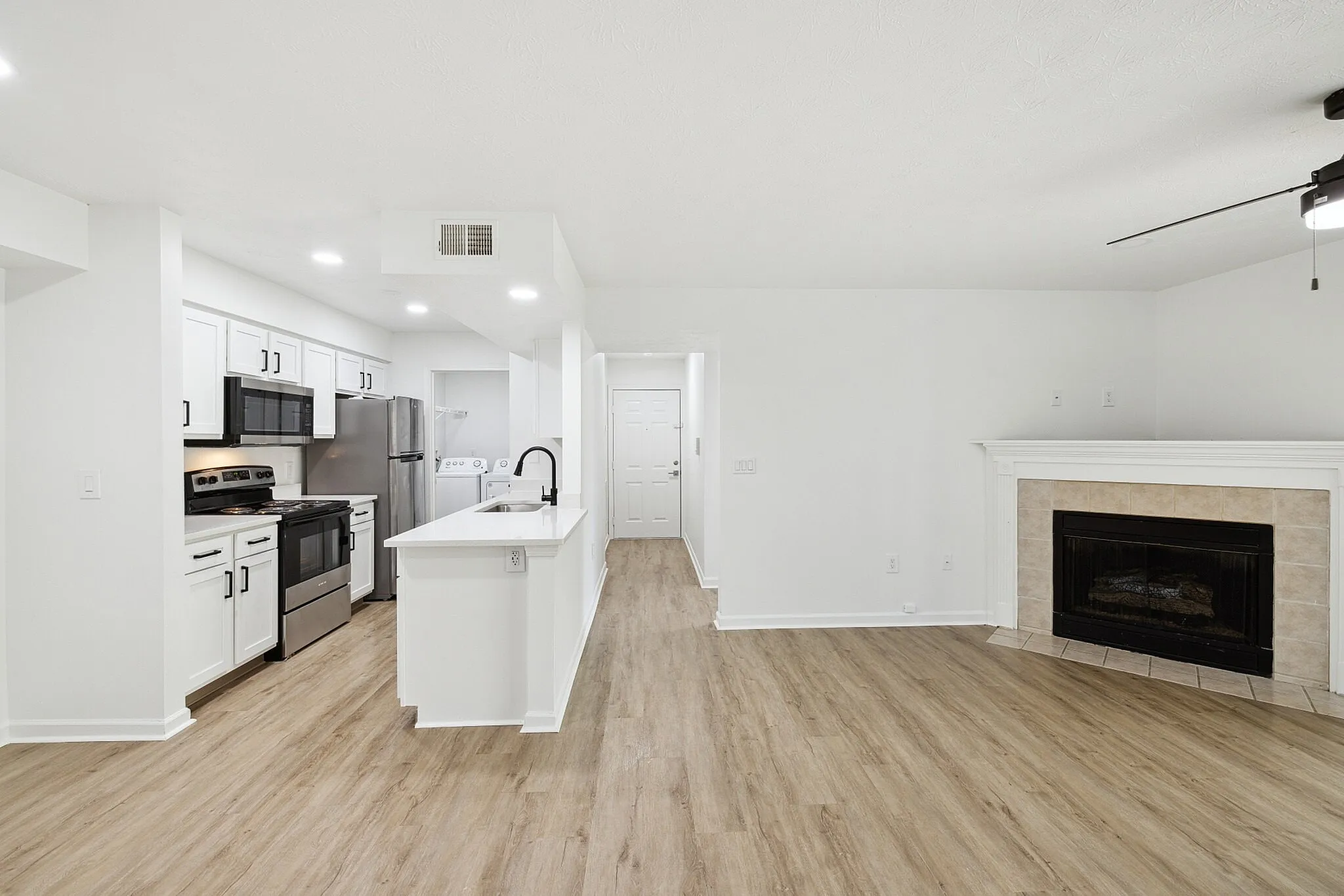 Modern open-concept apartment with sleek kitchen, stainless steel appliances, and inviting fireplace with elegant hardwood flooring.
