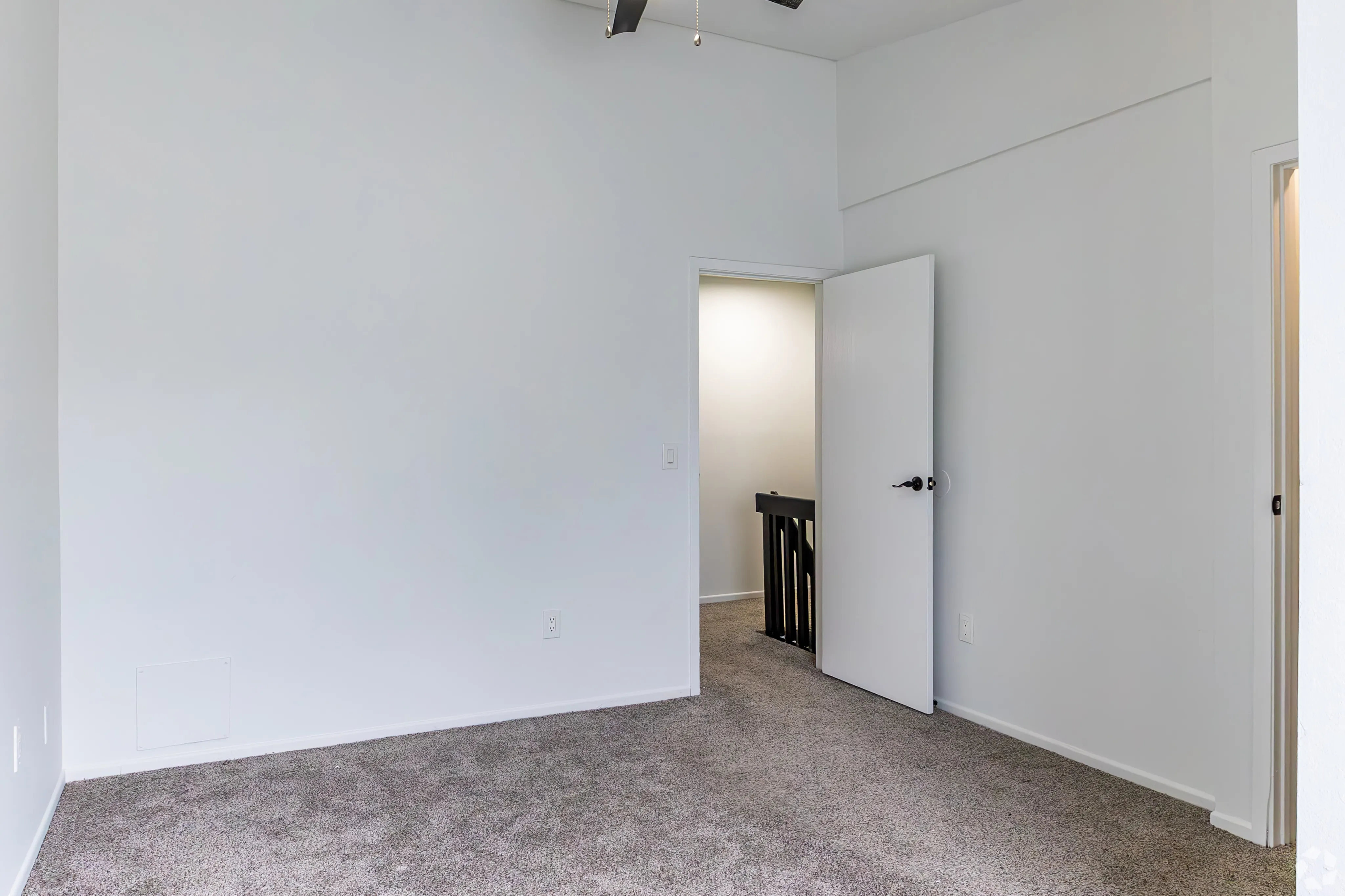 Bright and inviting room with plush carpet flooring, showcasing modern design and an open doorway leading to a well-lit hallway.