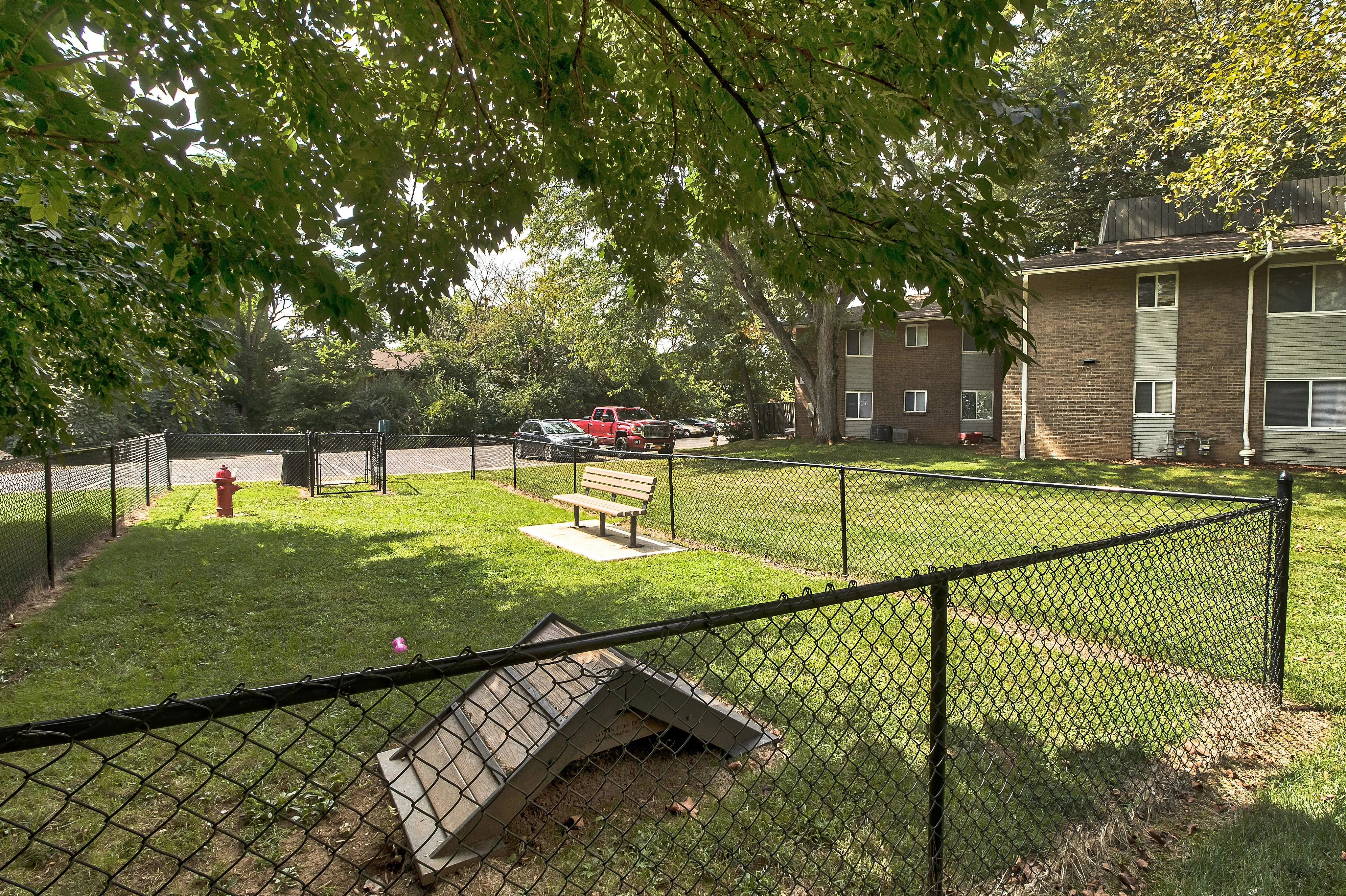 Charming apartment complex featuring a lush, fenced dog park with seating area and vibrant greenery.