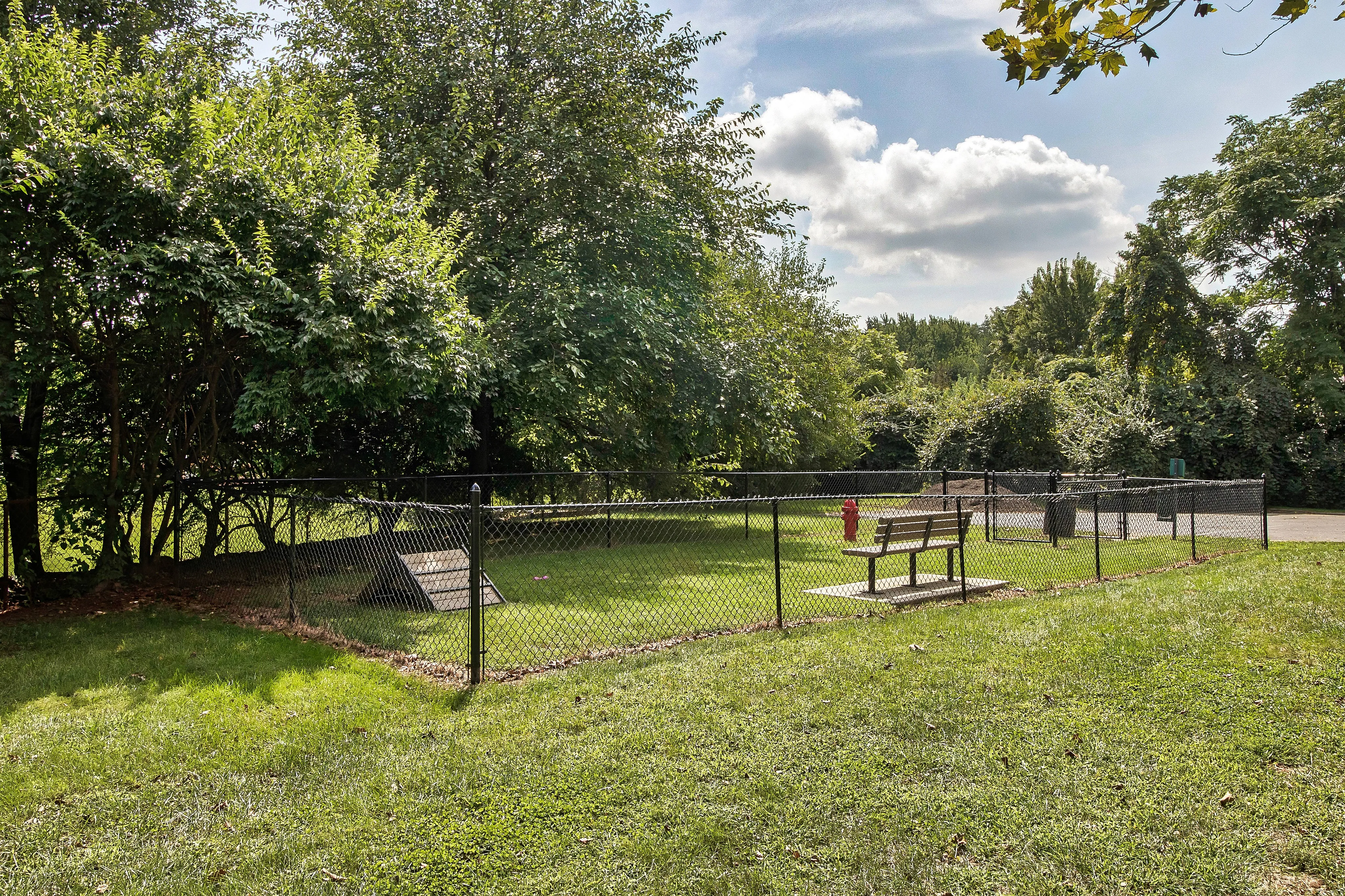Charming fenced dog park featuring lush greenery, a cozy bench, and a peaceful walking path ideal for relaxation and play.