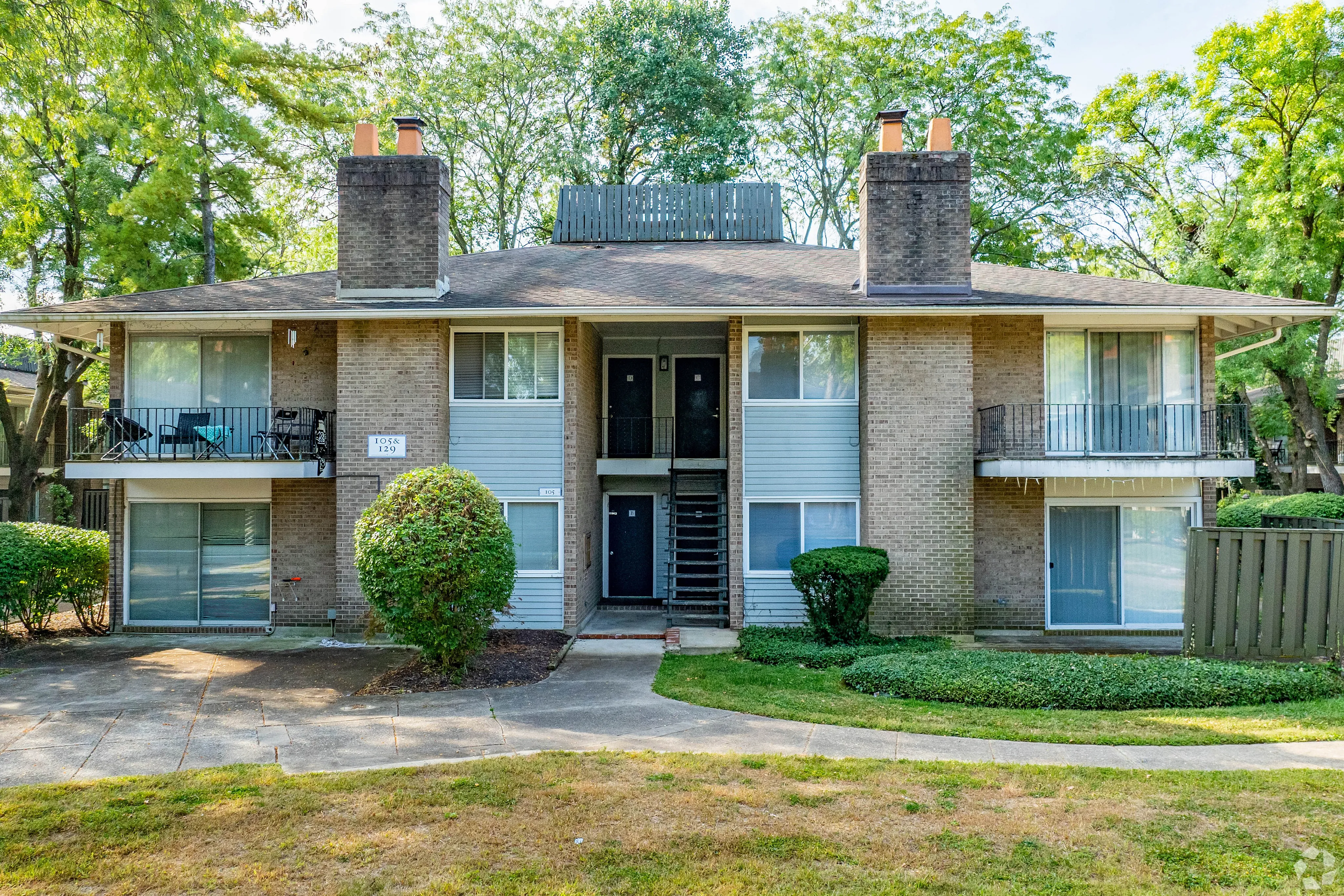 Charming two-story apartment building with spacious balconies and lush green surroundings.