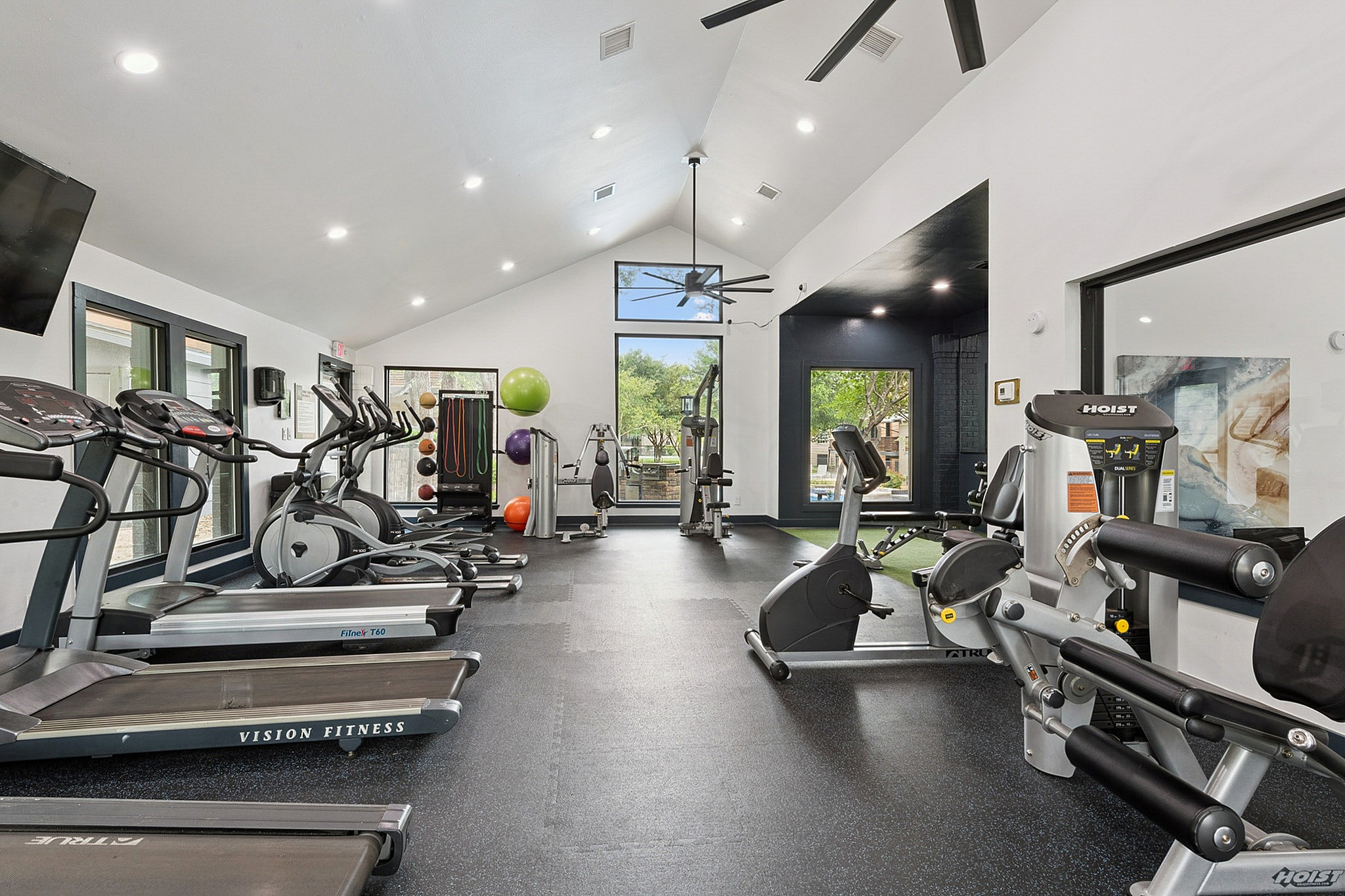 Modern fitness center with state-of-the-art exercise machines, bright natural lighting, and large windows overlooking lush greenery.